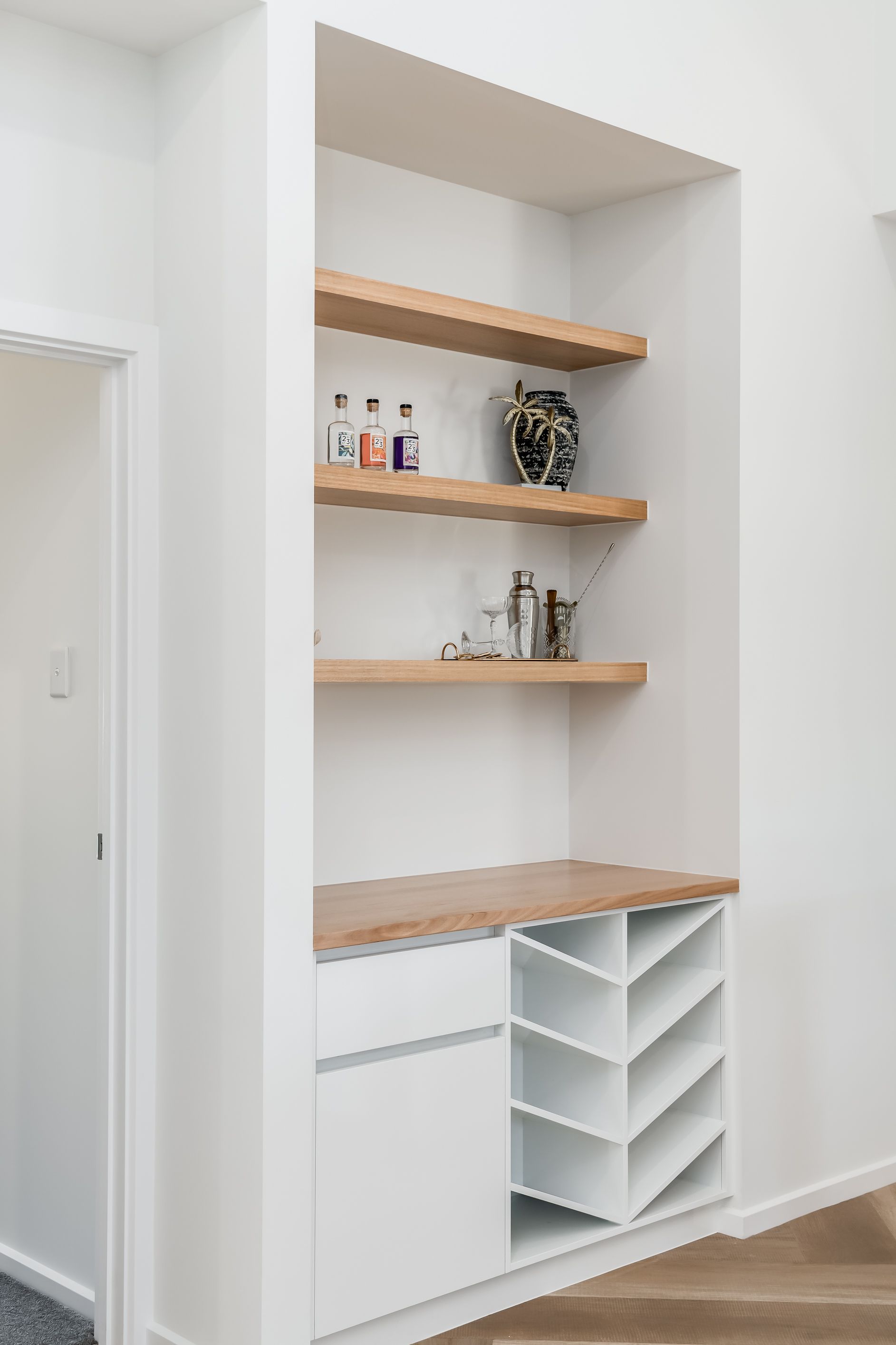Built-in white shelving nook with wooden shelves, countertop, and cubby storage in a bright hallway