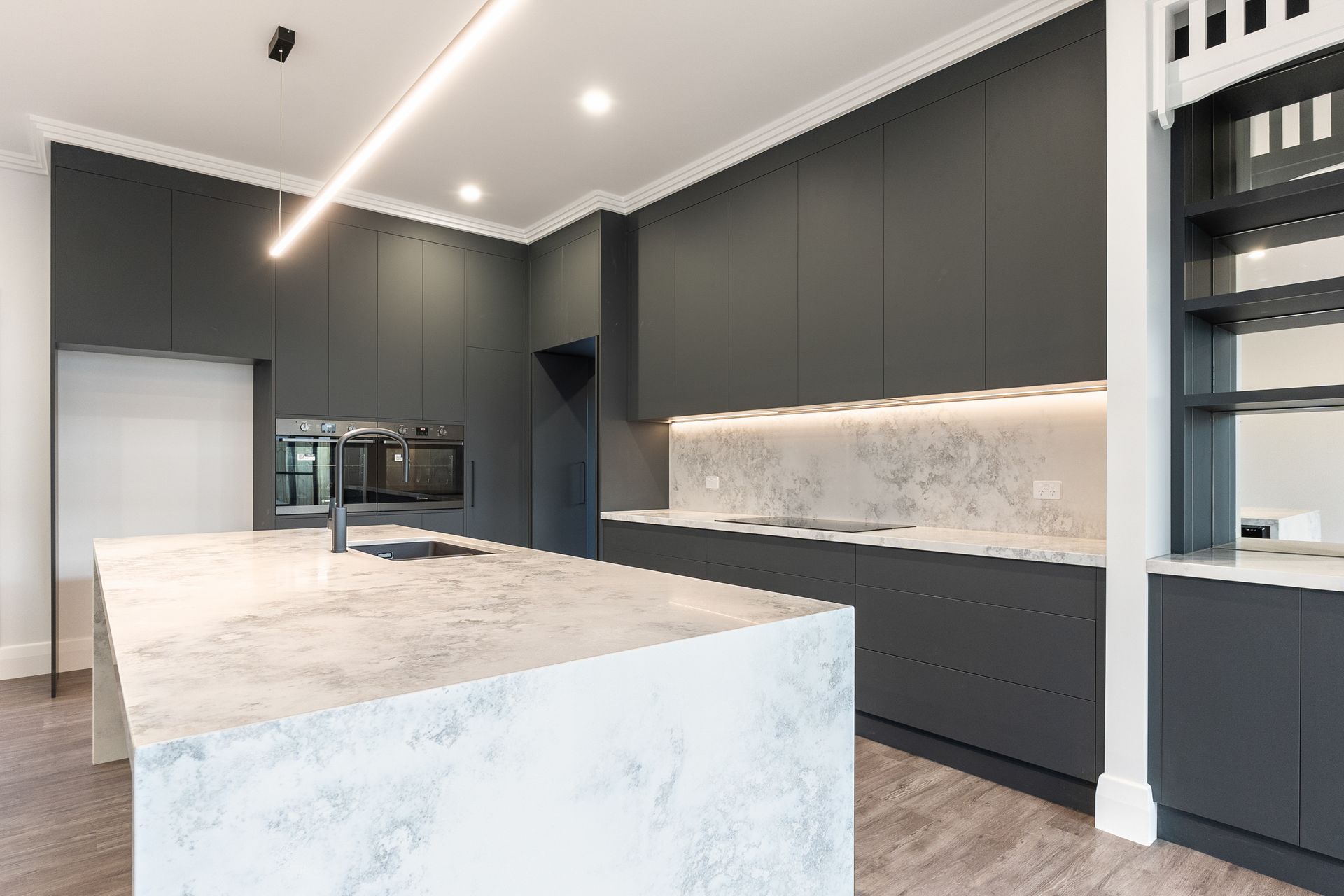 Modern gray kitchen with large marble island, recessed lighting, and built-in cabinets