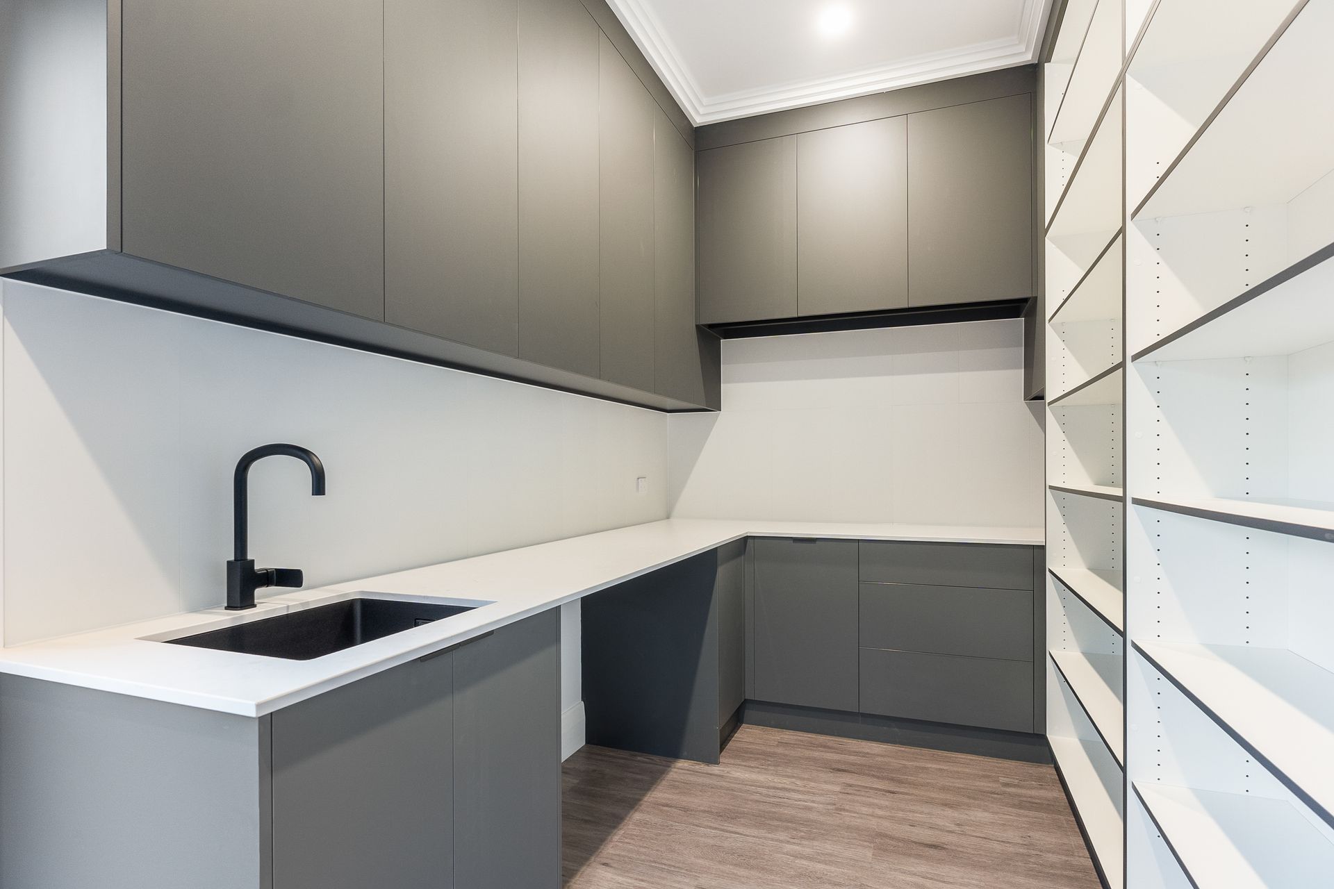 Modern L-shaped kitchen with gray cabinets, black sink and faucet, white countertops, and light wood flooring.