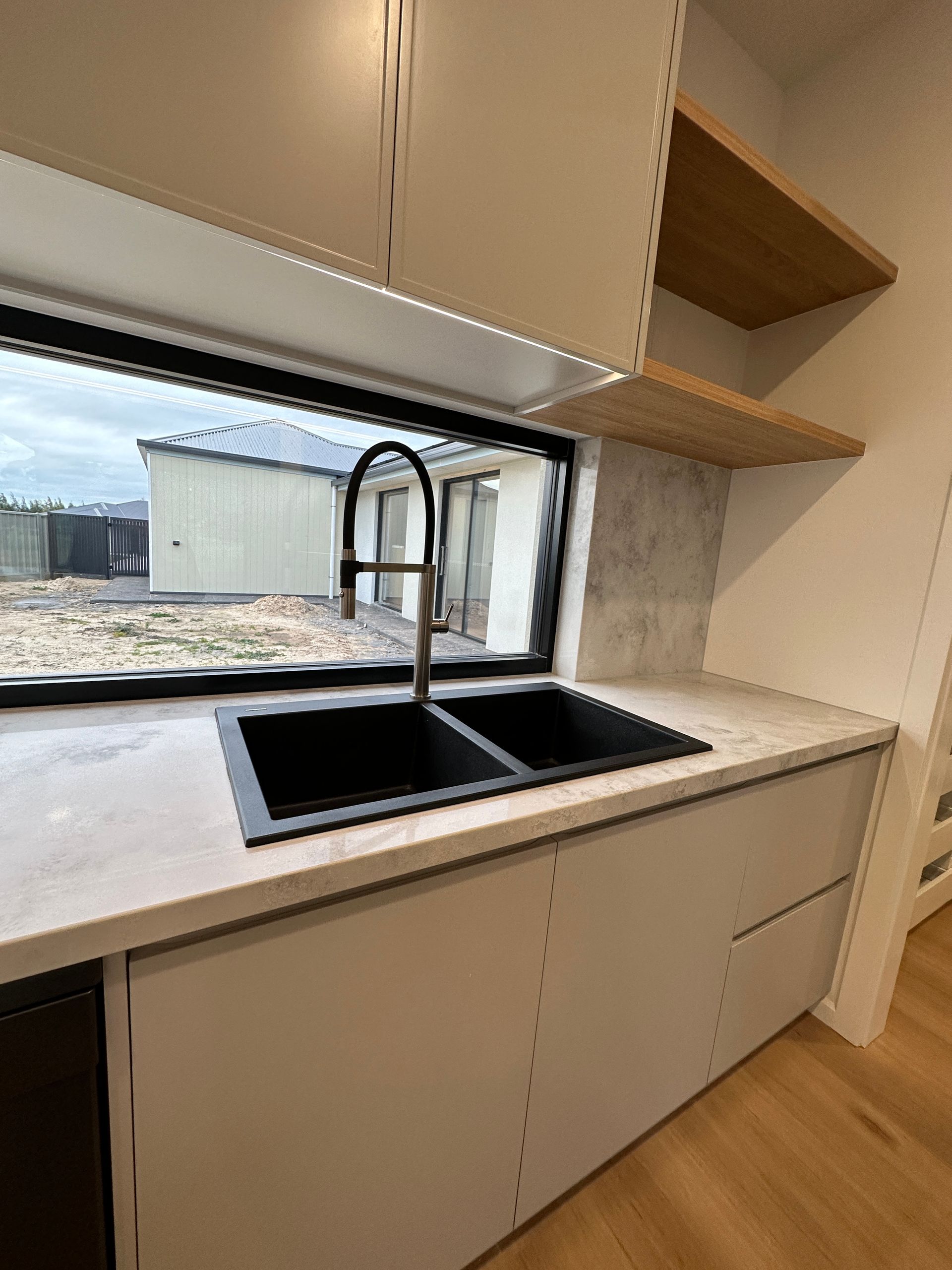 Modern kitchen sink with black faucet, light cabinets, and a window overlooking an outdoor area