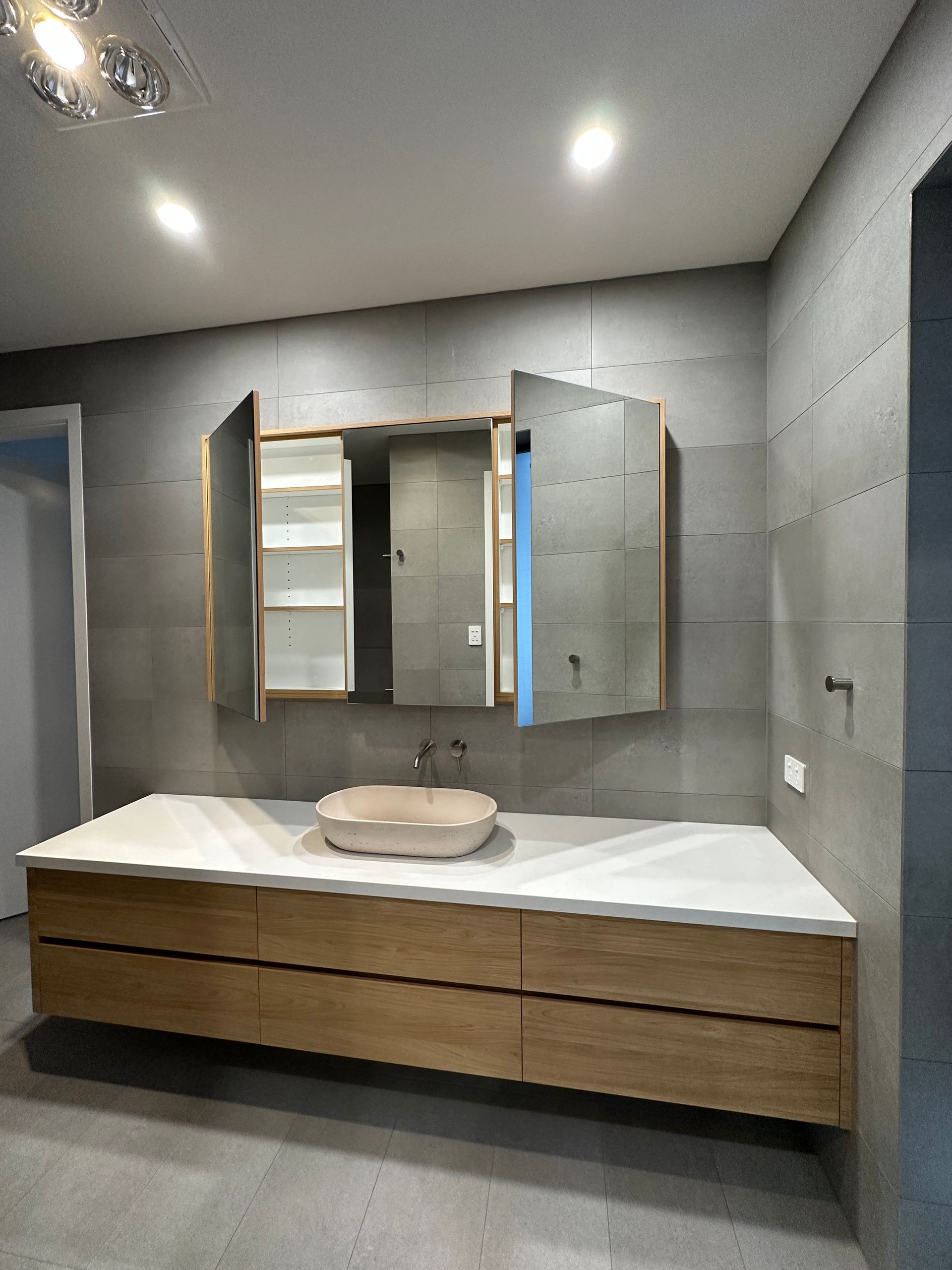 Modern bathroom vanity with double mirrored cabinets, white sink, and wood drawers under recessed lighting