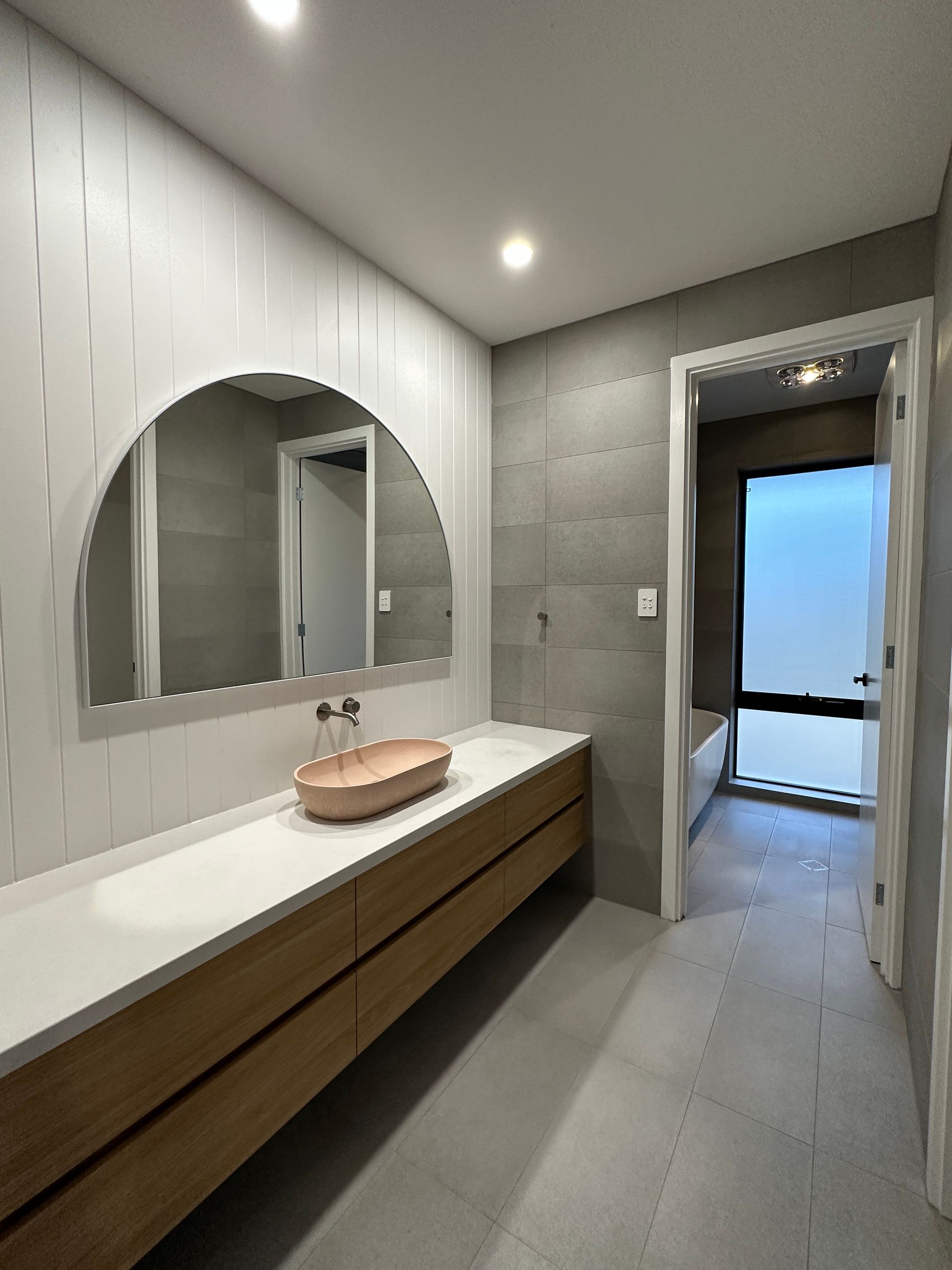 Modern bathroom with double sink vanity, oval mirror, and frosted glass door to a bright balcony.