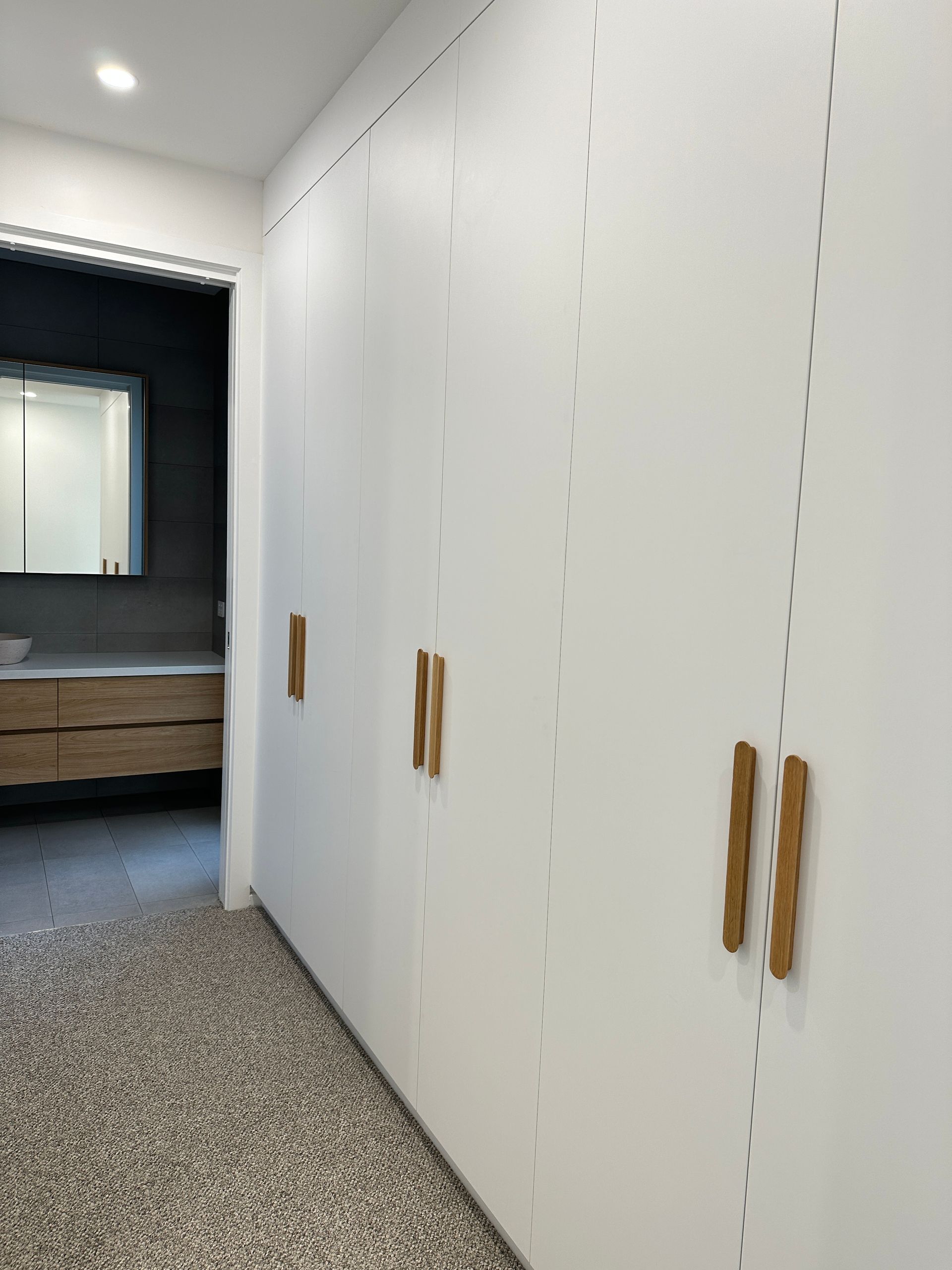 White closet doors with wooden handles in a carpeted hallway beside a bathroom vanity.