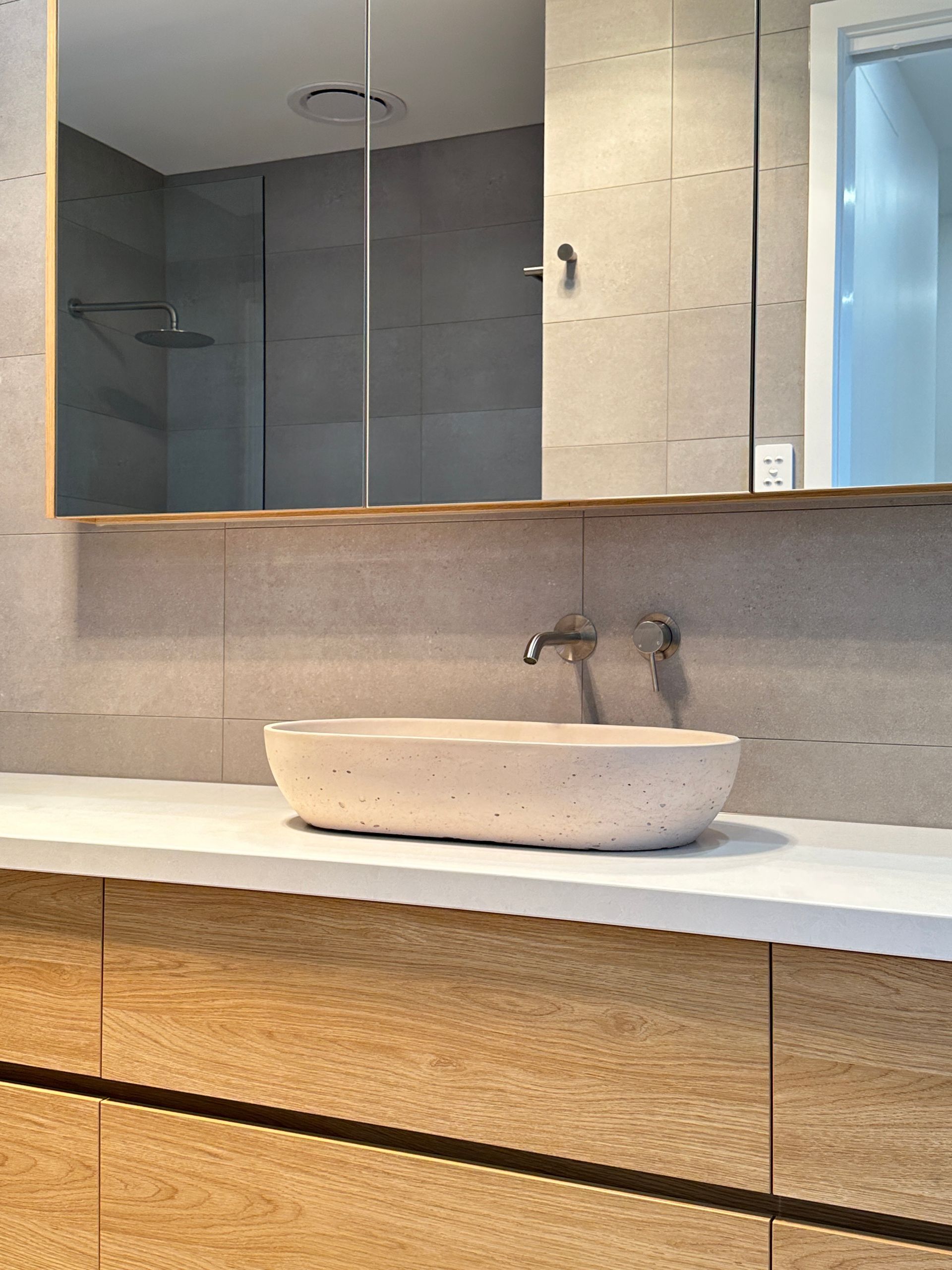 Modern bathroom vanity with round stone sink, wall faucet, and large mirror above wood cabinets.