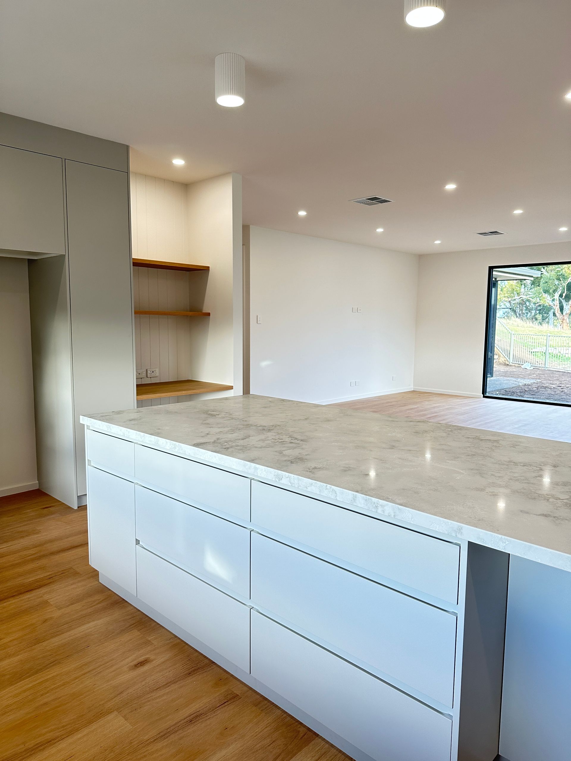 Modern kitchen with white cabinets, marble island, wood floors, and built-in shelving.