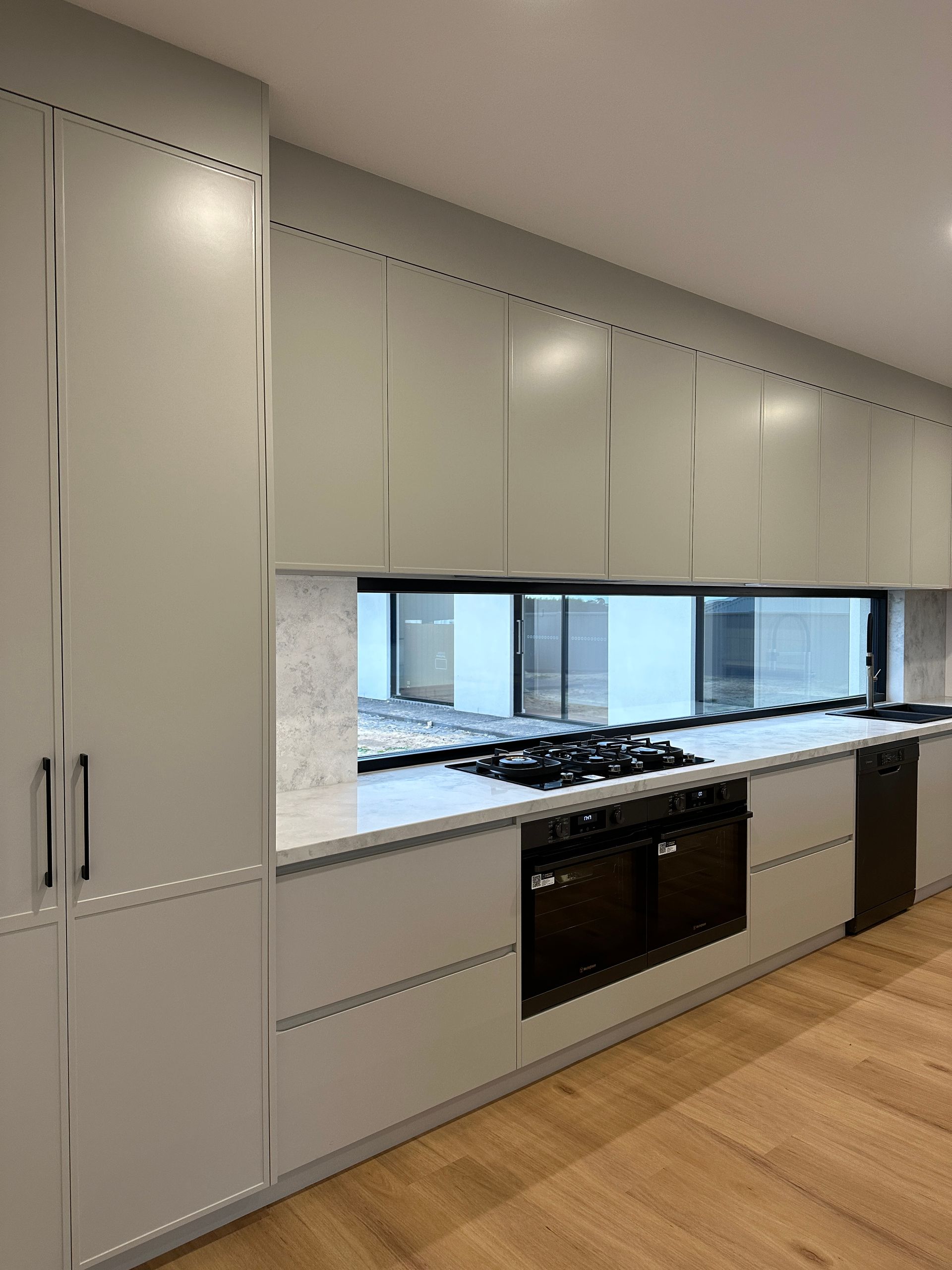 Modern white kitchen with built-in oven, gas cooktop, and wood flooring