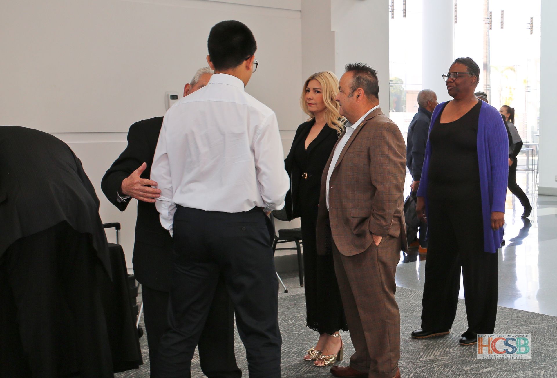A group of people are standing in a room with a hcsb logo in the corner