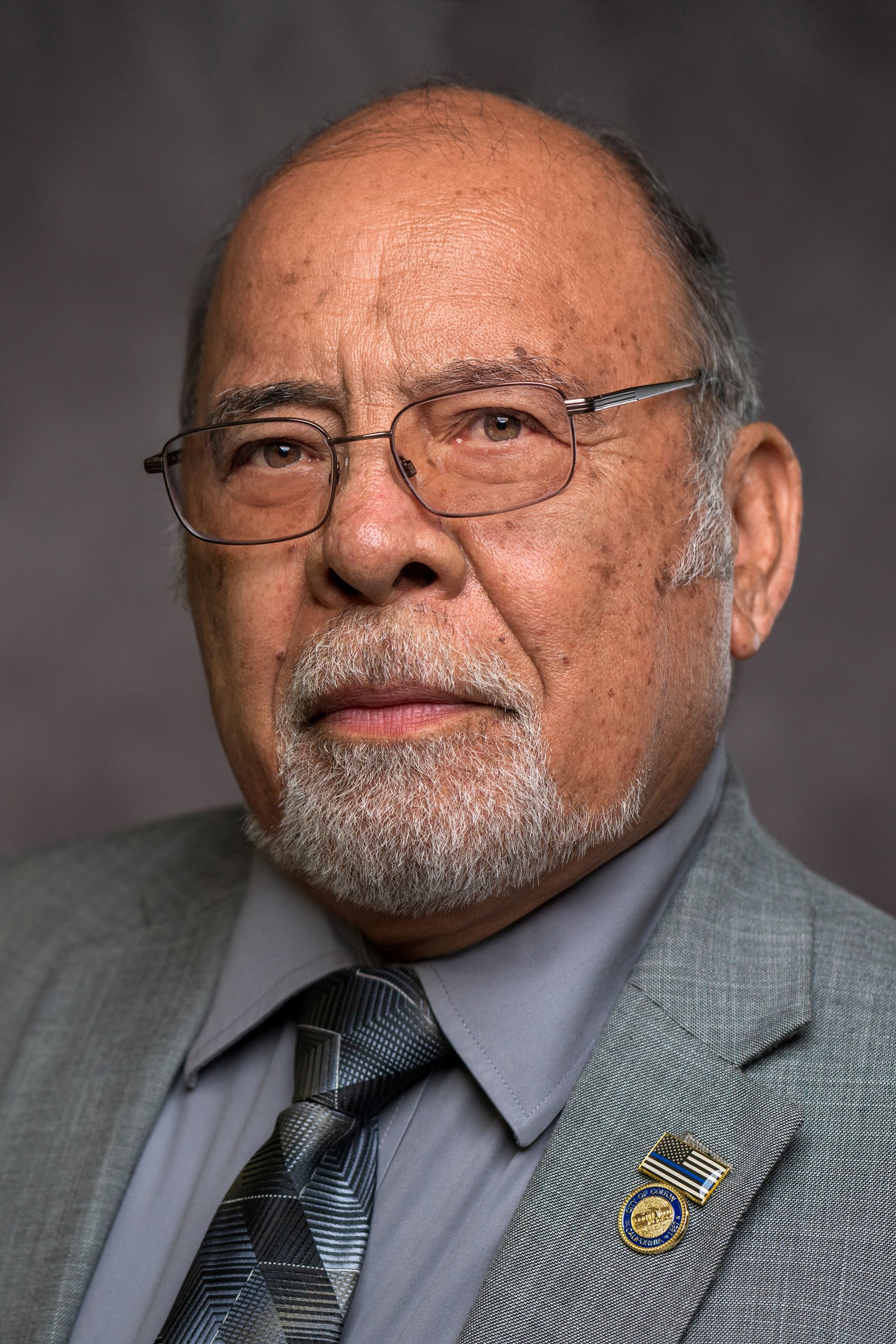 A man with a beard and glasses is wearing a suit and tie.