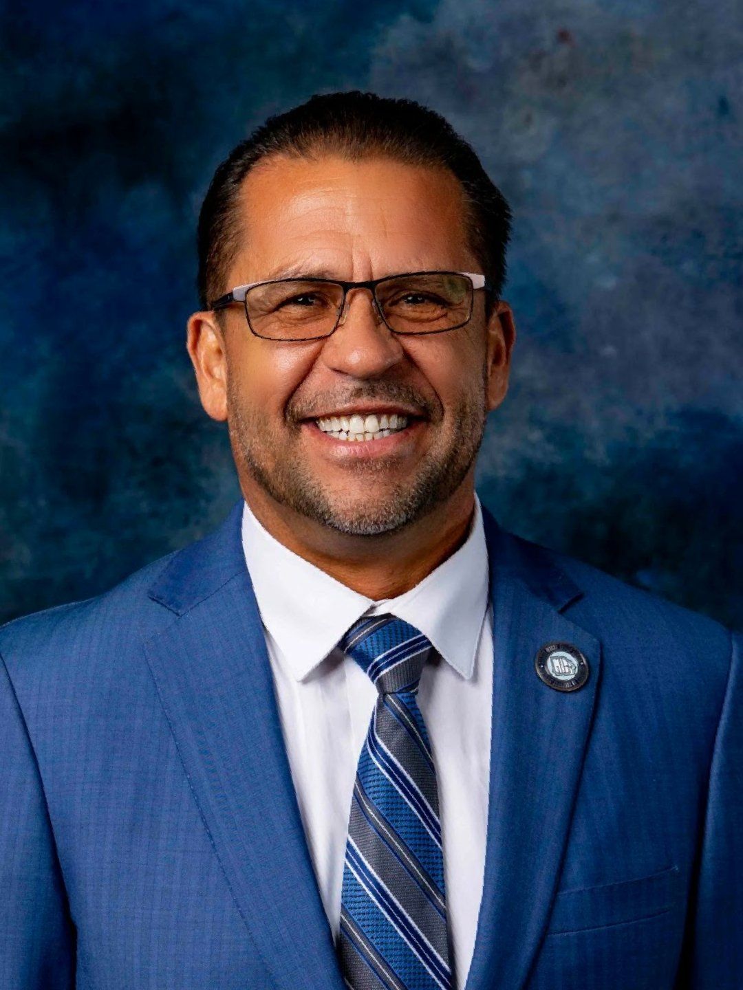 A man in a blue suit and tie is smiling for the camera.