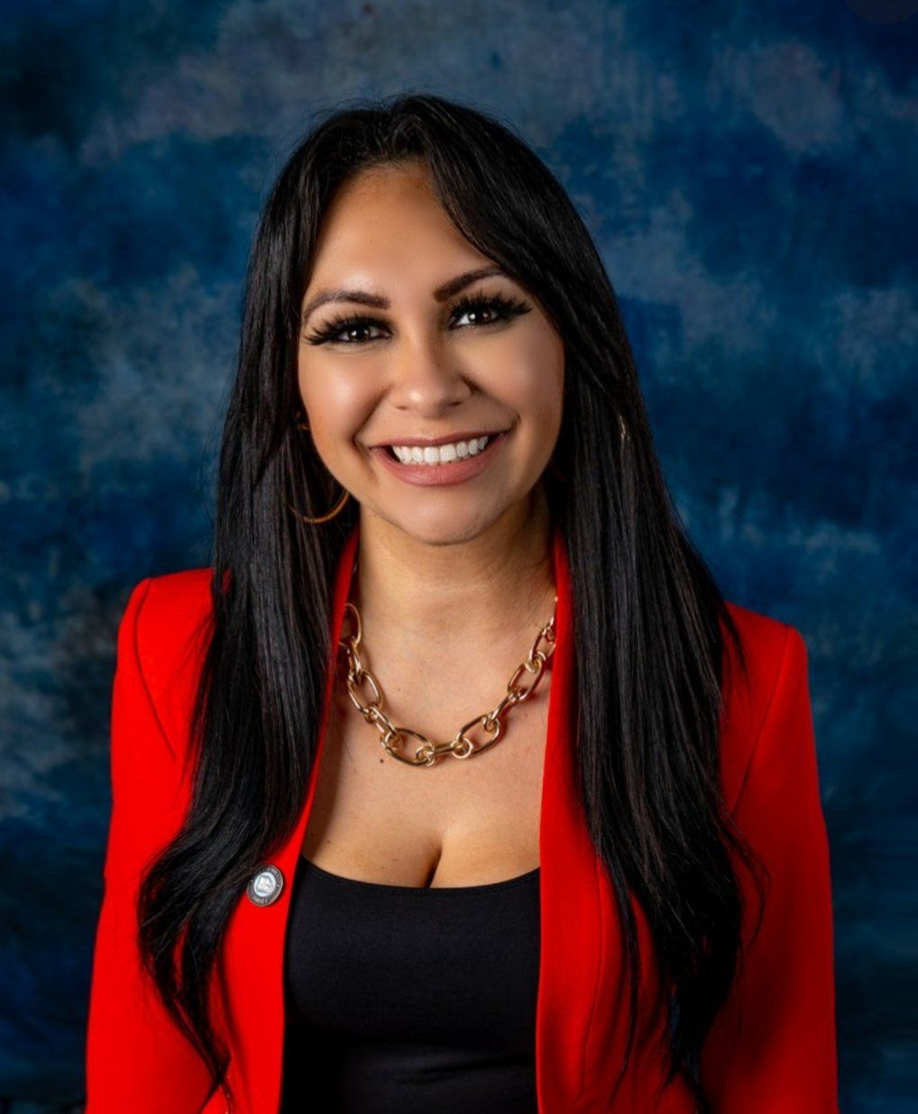 A woman wearing a red jacket and a gold necklace is smiling for the camera.
