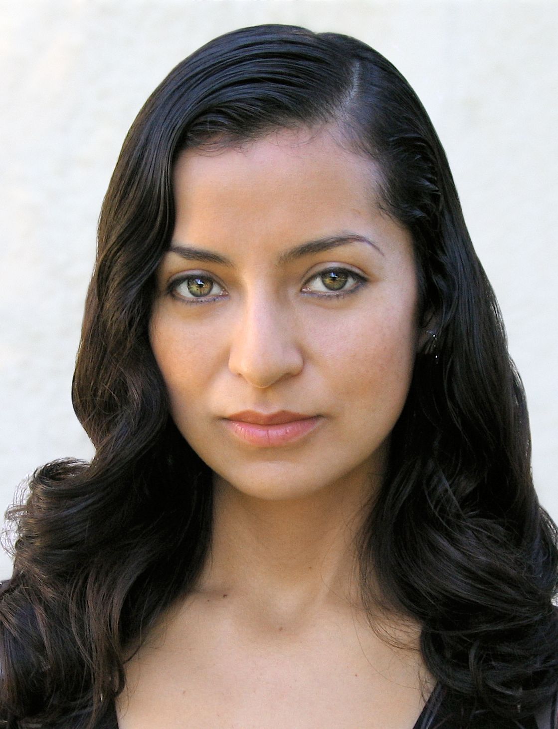 A woman with long dark hair and green eyes looks at the camera