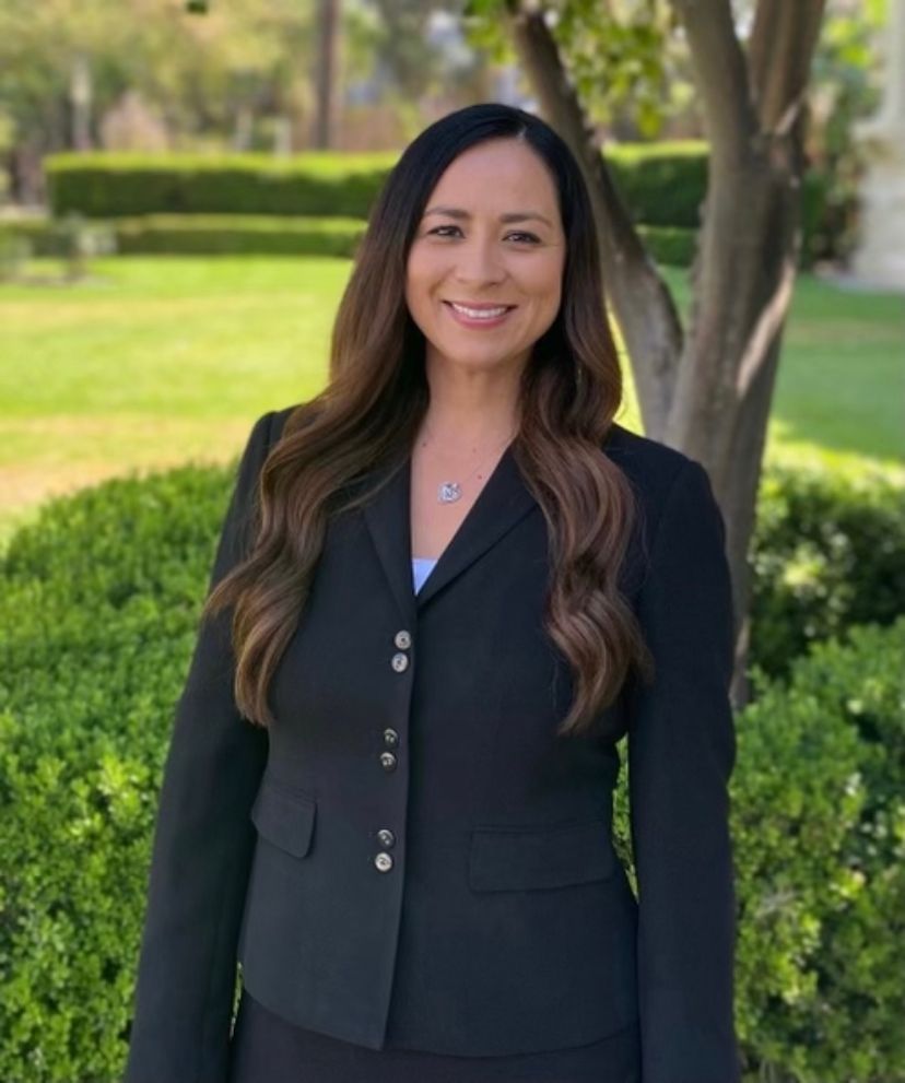 A woman in a black suit is standing in front of a tree.