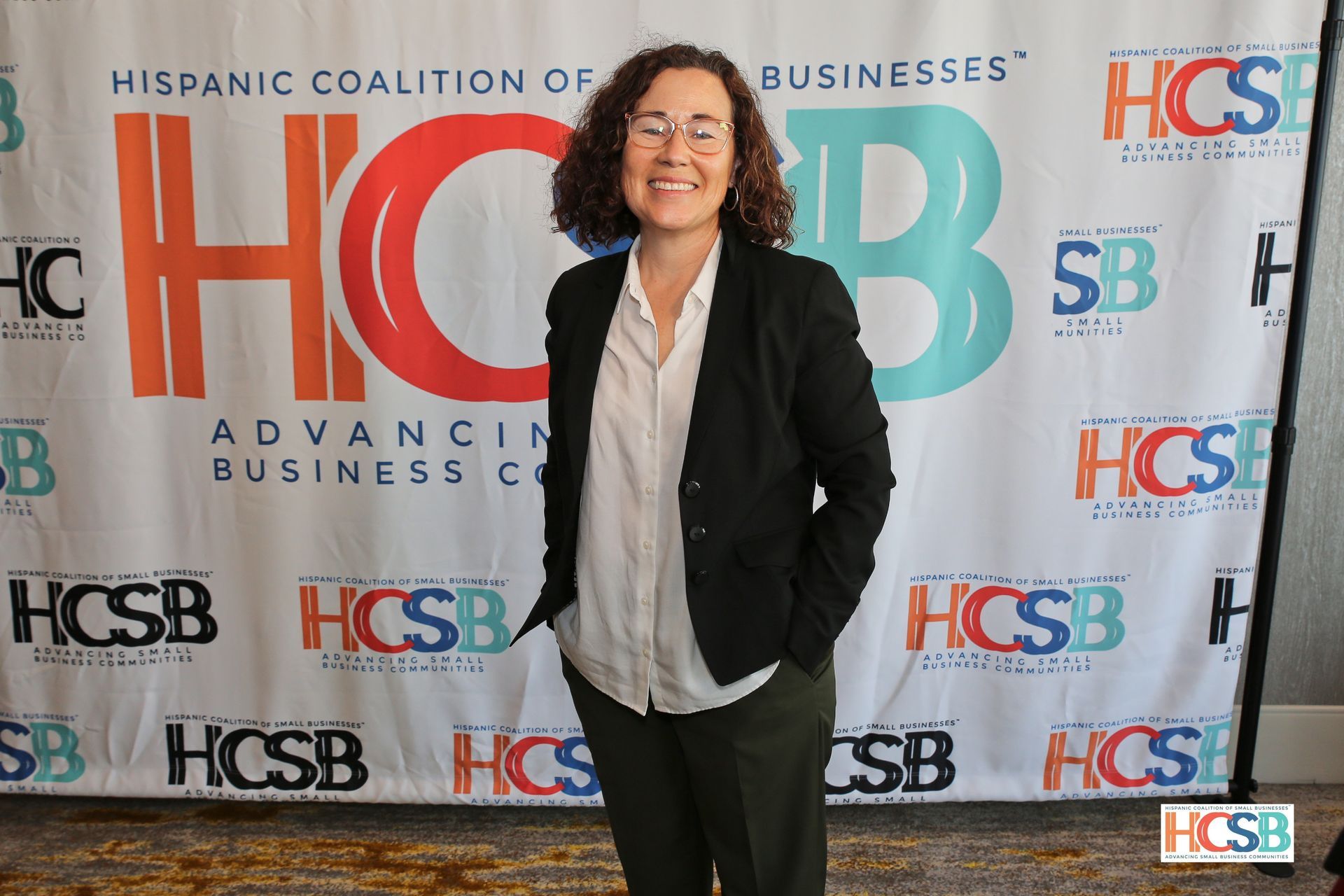 A woman is standing in front of a hispanic coalition of businesses banner.