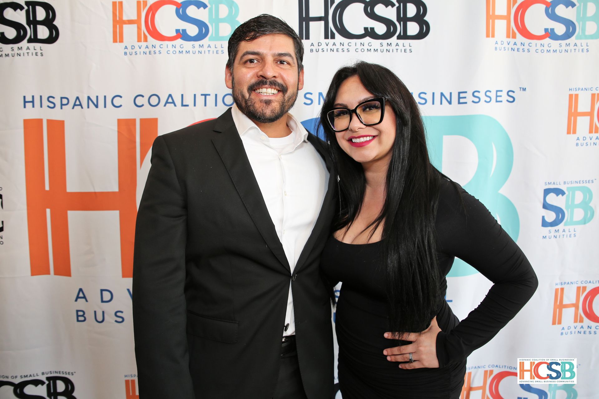 A man and a woman are posing for a picture in front of a wall that says hispanic coalition
