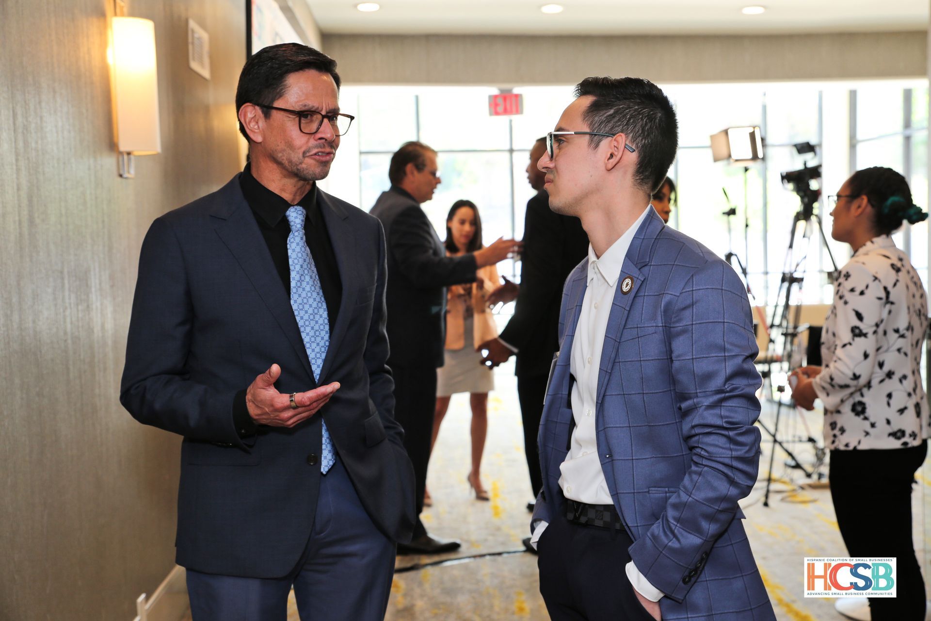 Two men in suits and ties are talking to each other in a hallway.