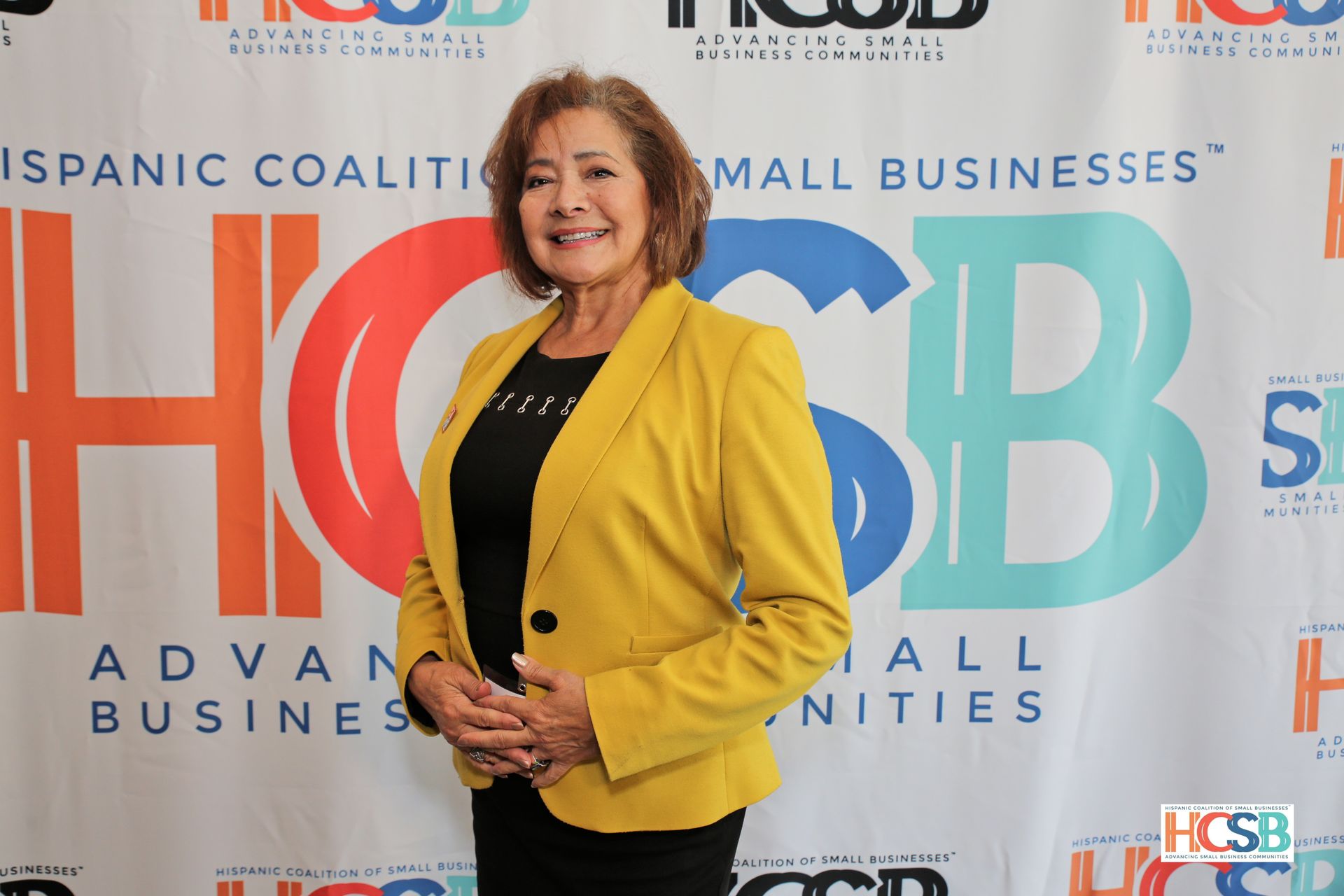 A woman in a yellow jacket is standing in front of a sign that says hispanic coalition small businesses