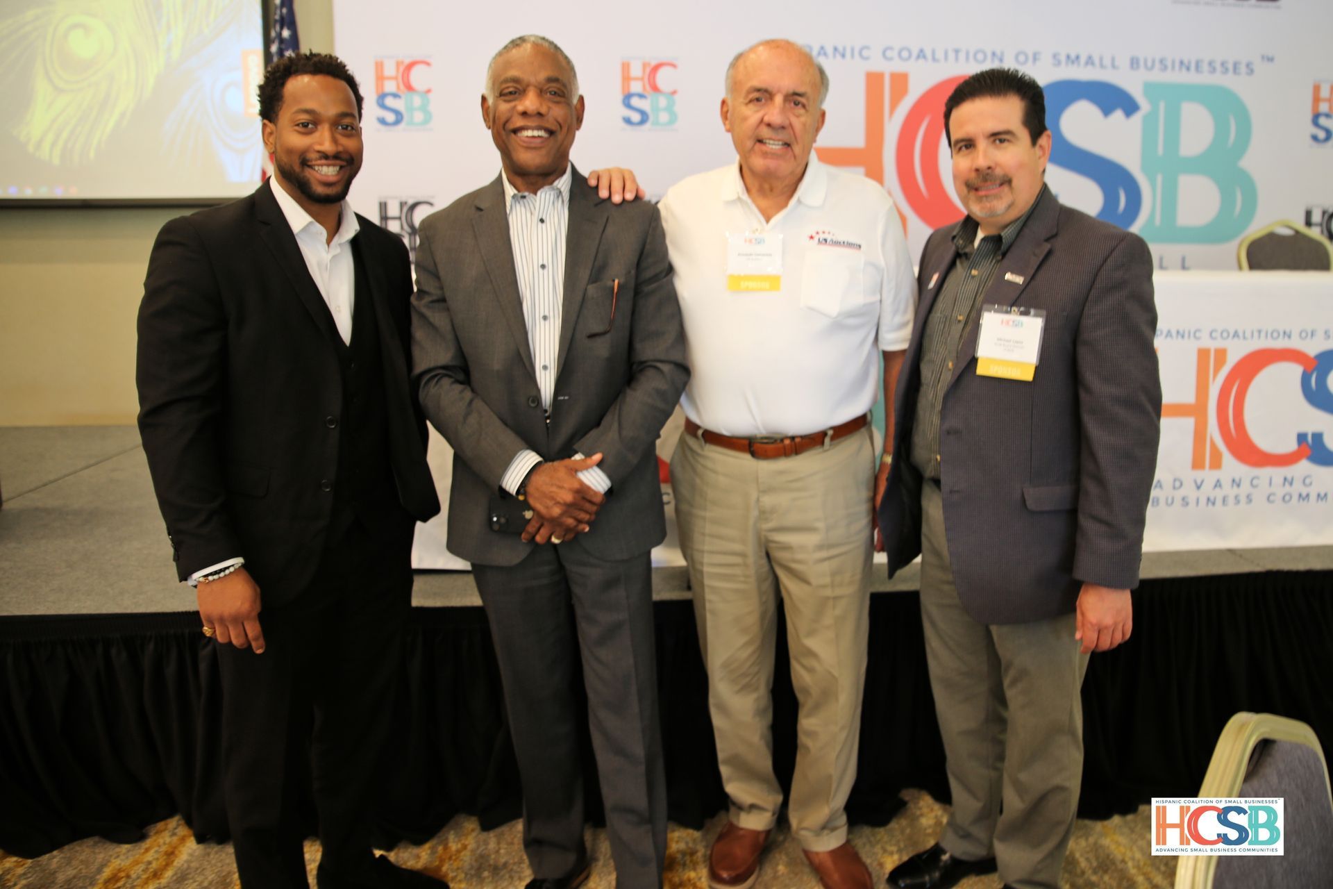 Four men are posing for a picture in front of a sign that says hcsb