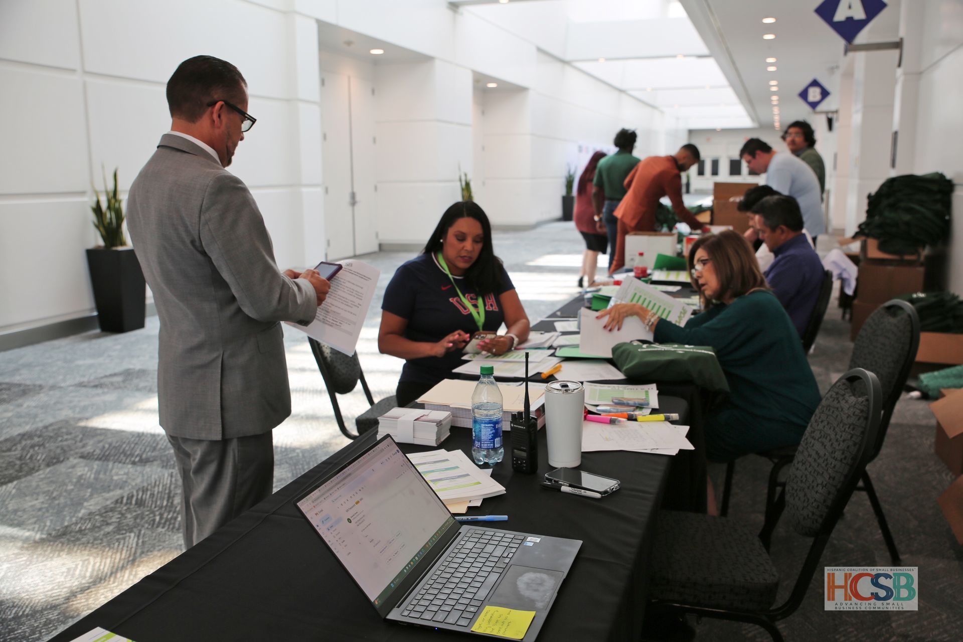 A group of people are standing around a table with a laptop on it