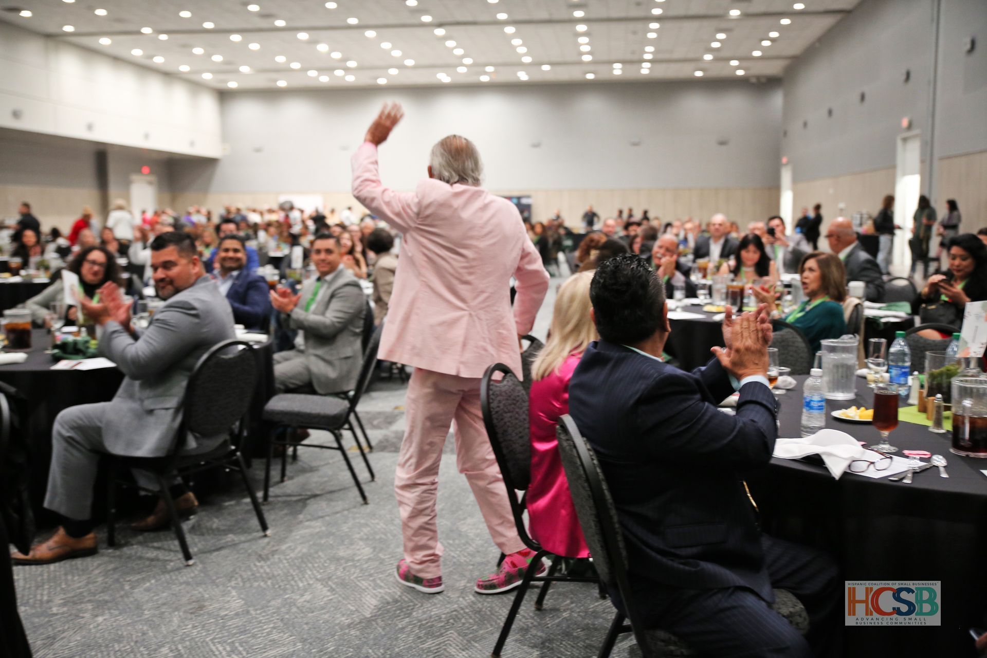 A man in a pink suit is dancing in front of a crowd at a conference.