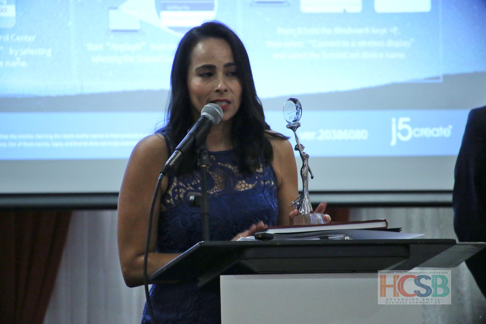 A woman in a blue dress is standing at a podium speaking into a microphone ..