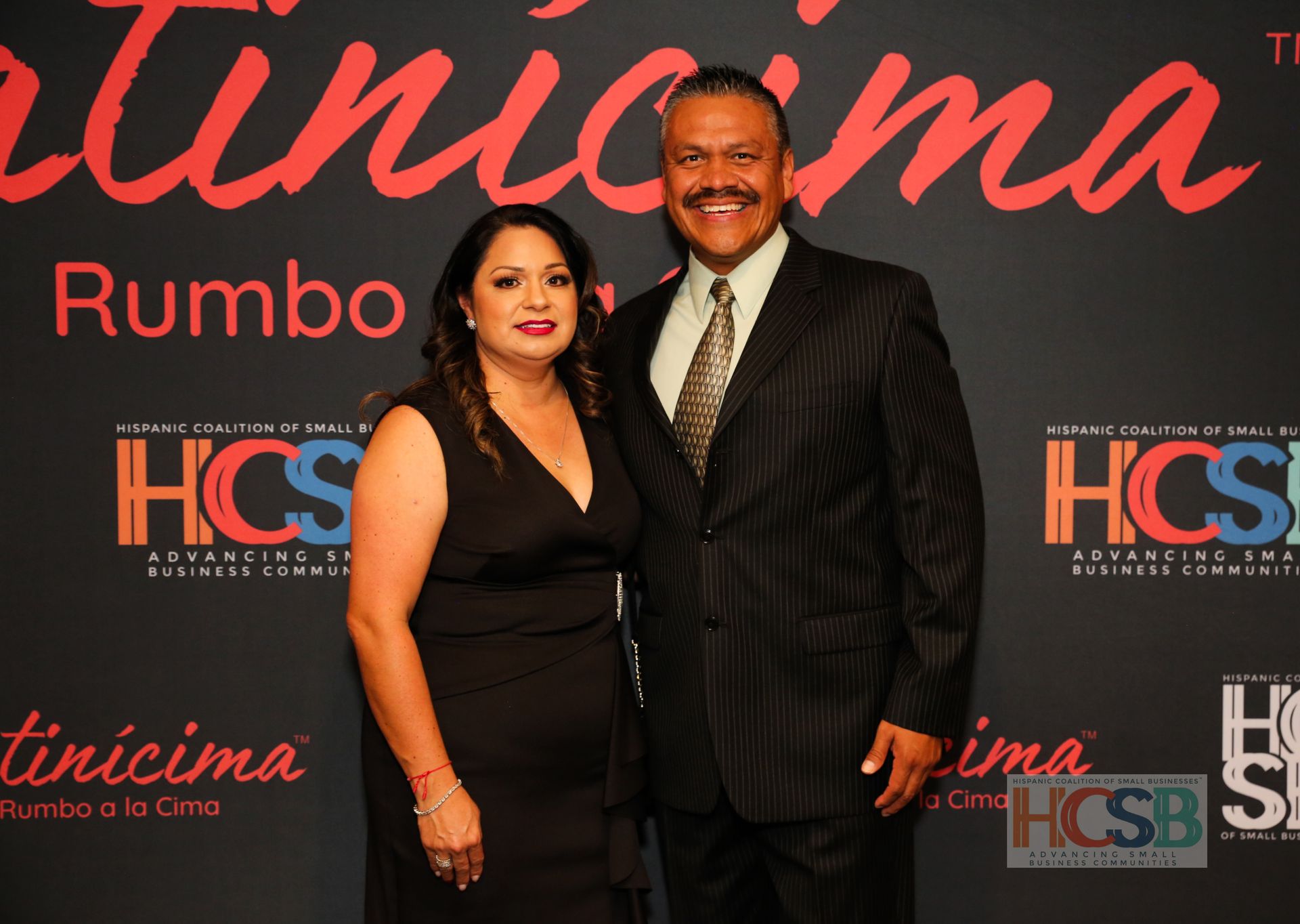 A man and a woman are posing for a picture in front of a wall that says hcsb