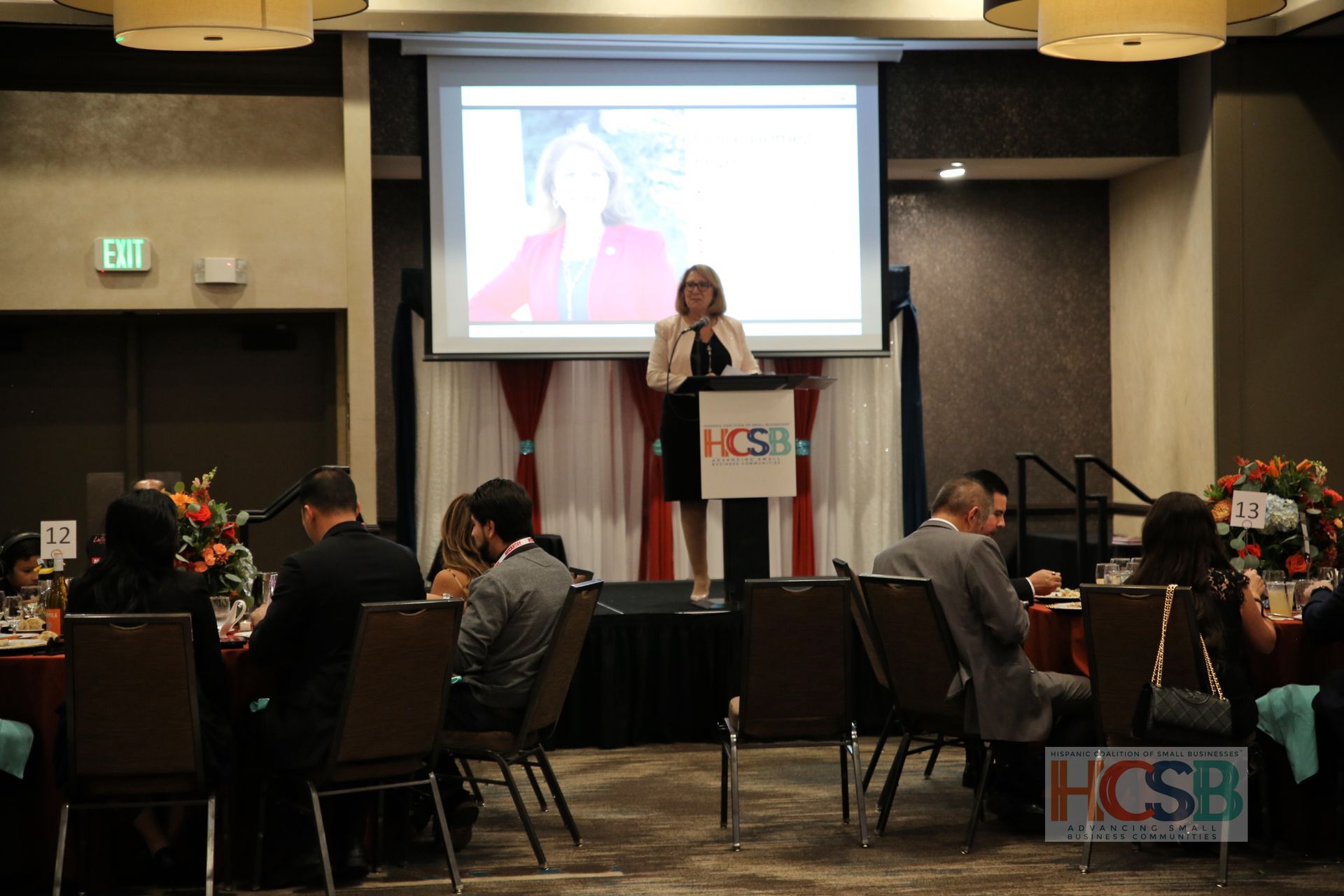 A woman is giving a speech at a podium in front of a projector screen.