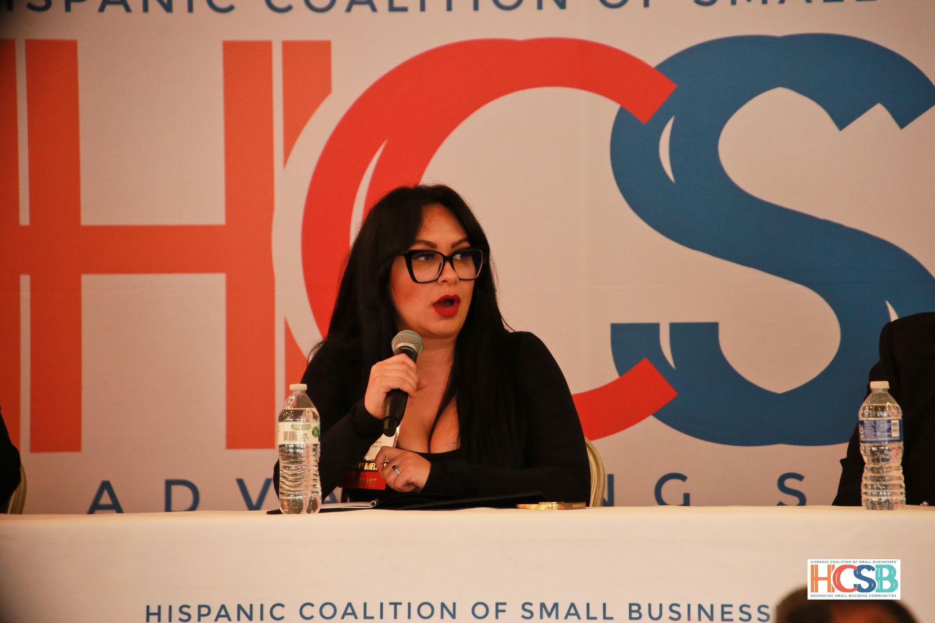 A woman speaking into a microphone at a hispanic coalition of small business event