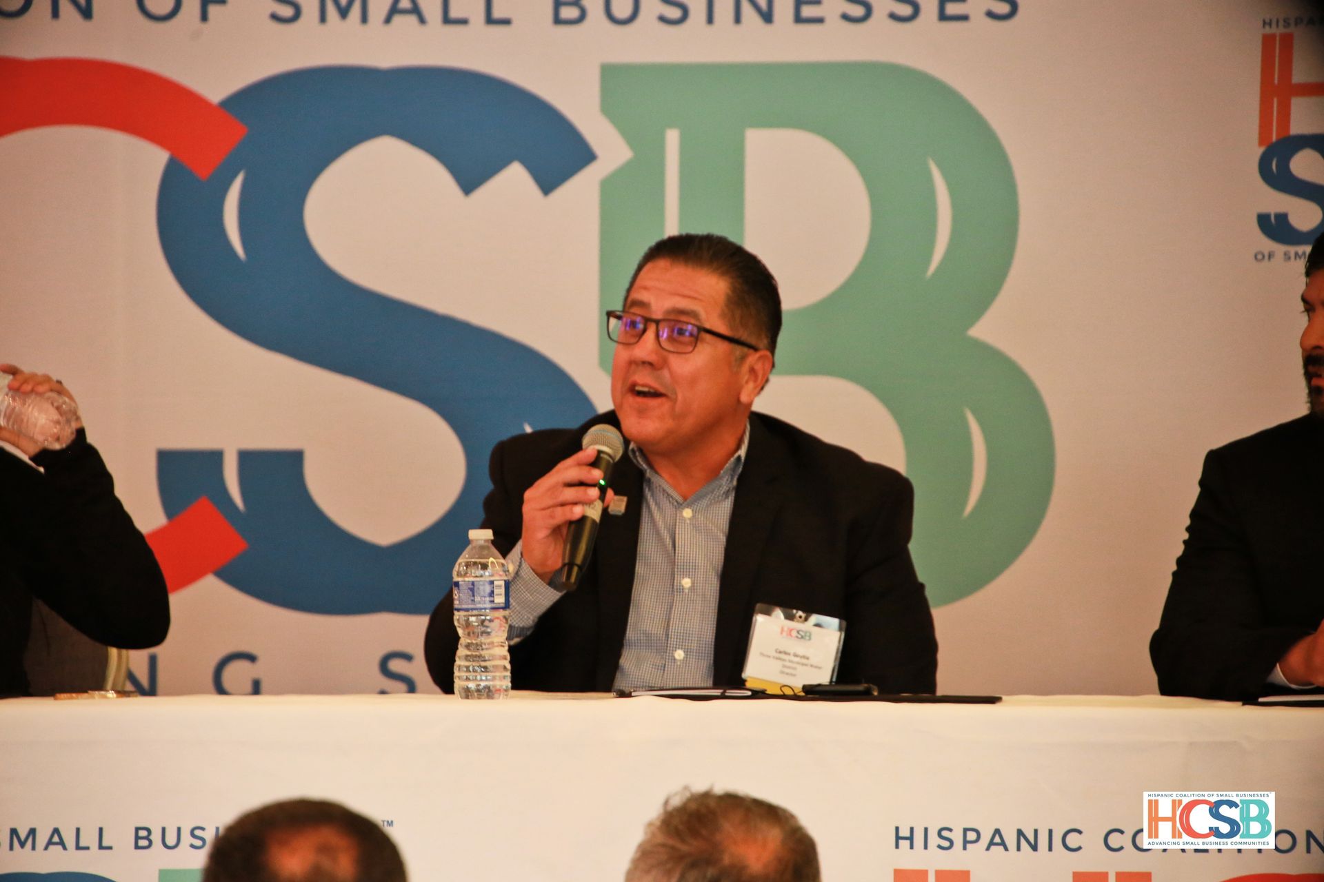 A man is speaking into a microphone in front of a sign that says csb