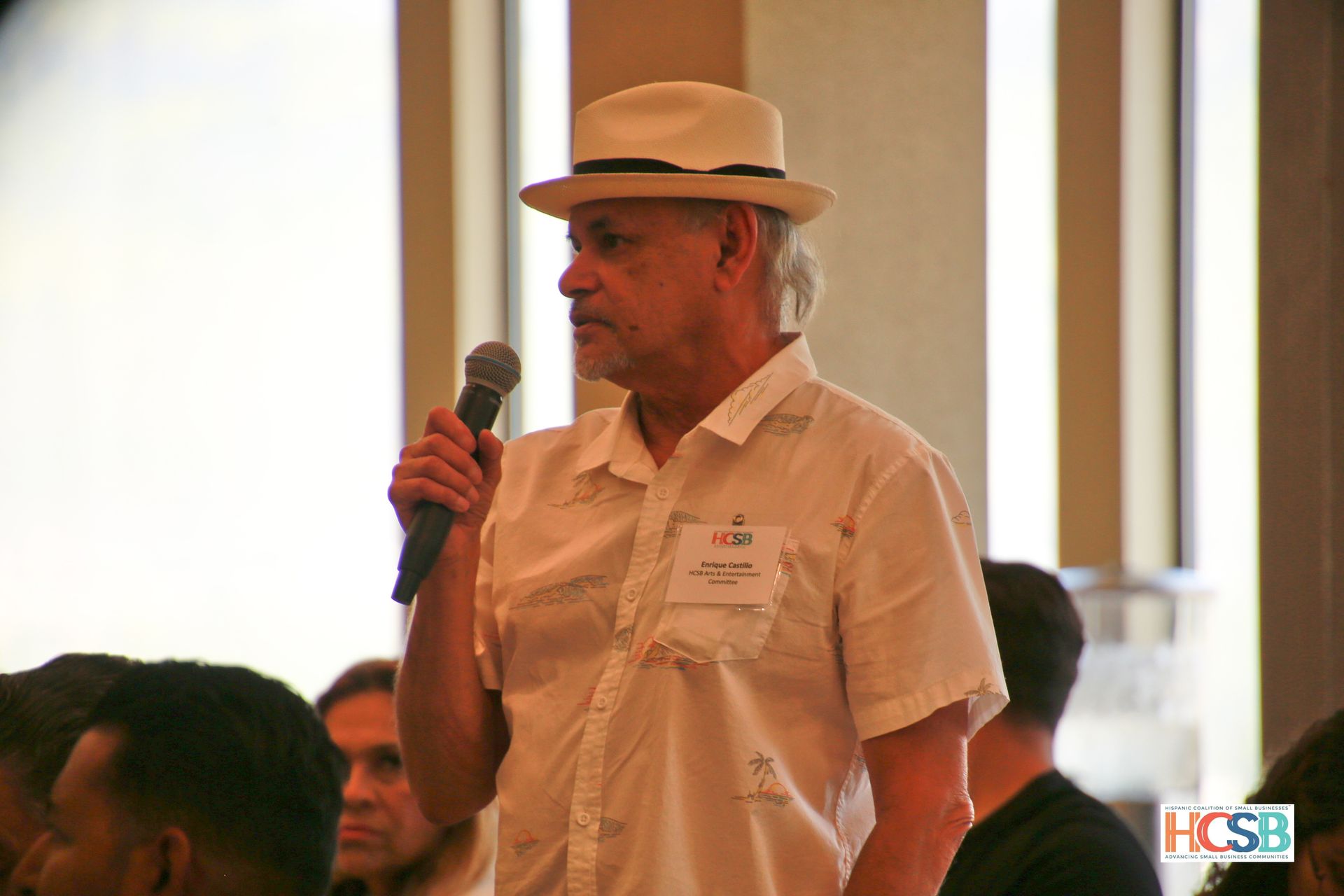 A man in a hat is holding a microphone in front of a group of people.