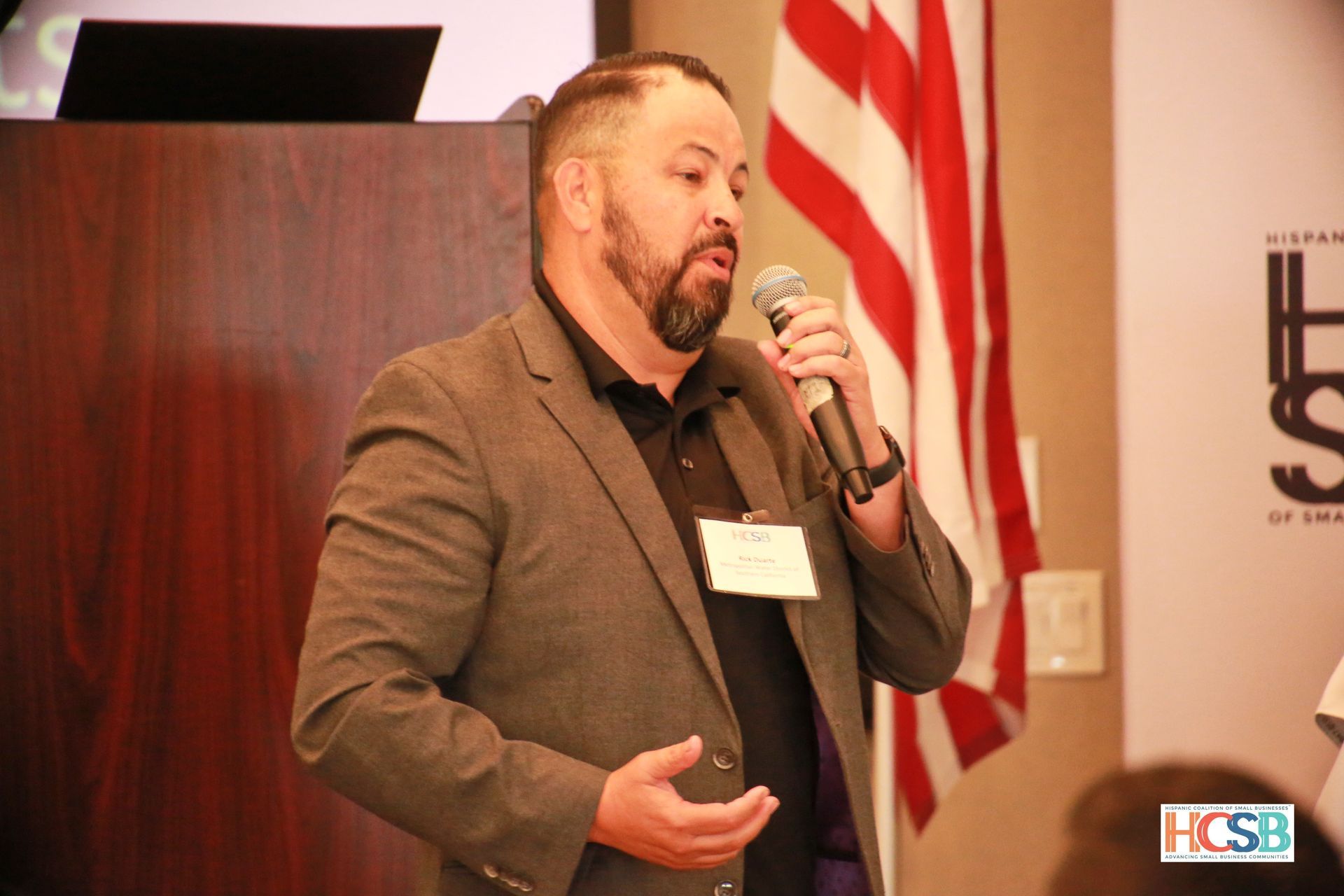 A man in a suit is holding a microphone in front of an american flag.