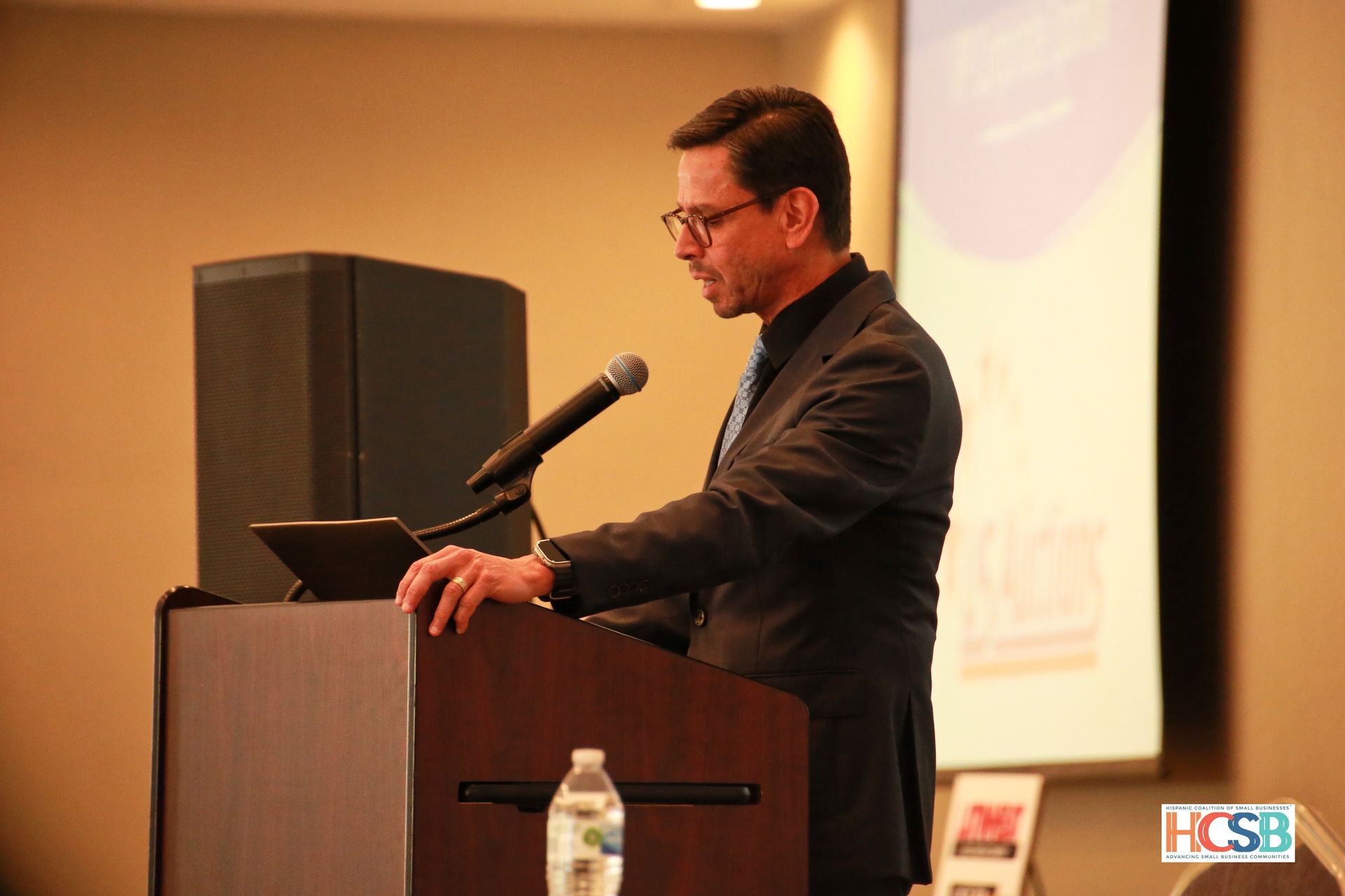 A man in a suit stands at a podium giving a speech
