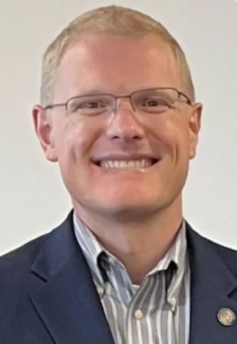 A man wearing glasses and a suit is smiling for the camera.