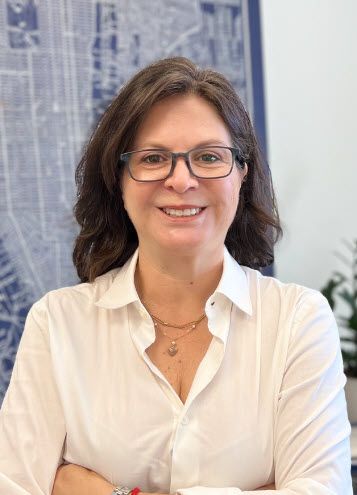 A woman wearing glasses and a white shirt is smiling for the camera.