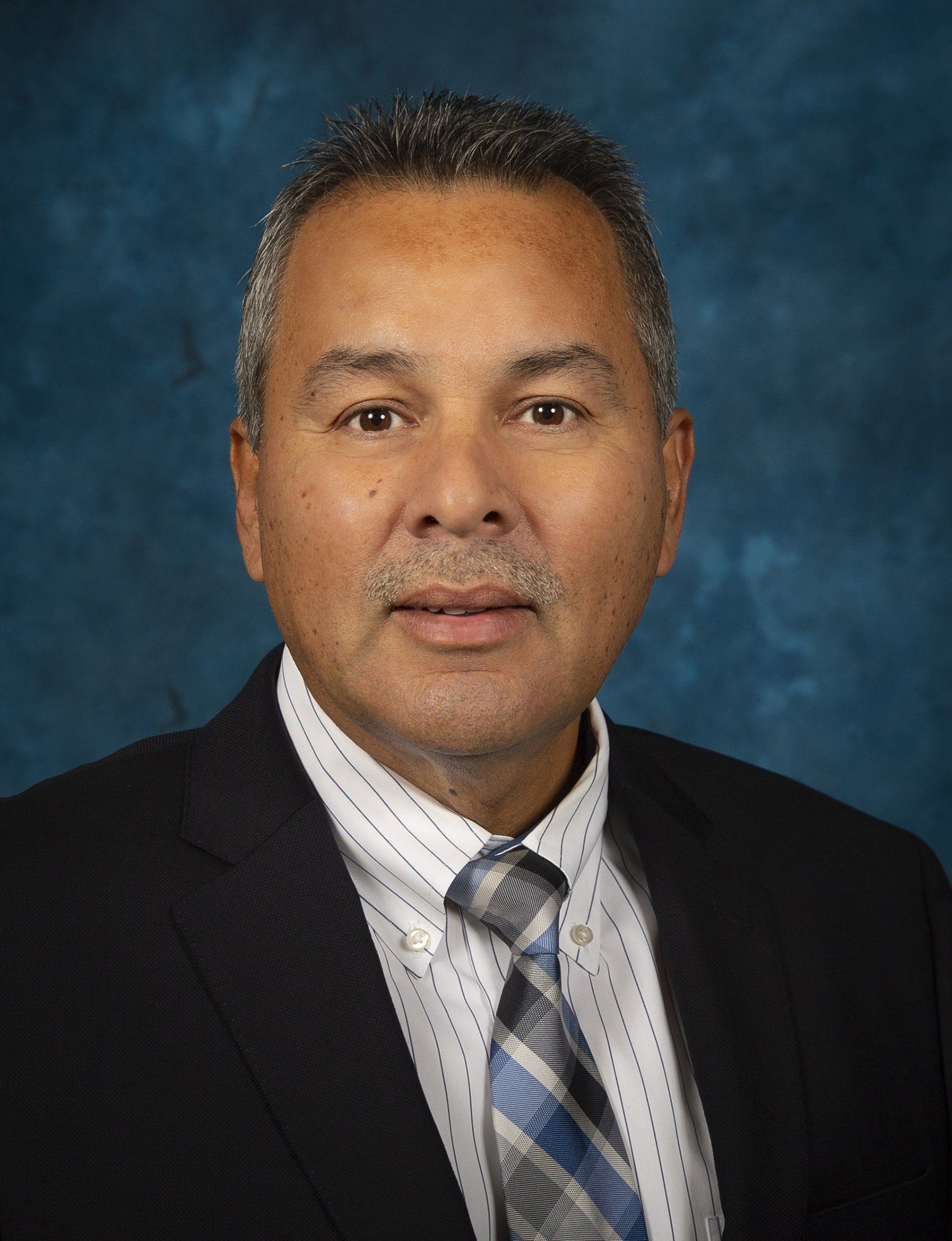 A man in a suit and tie is standing in front of a blue background.