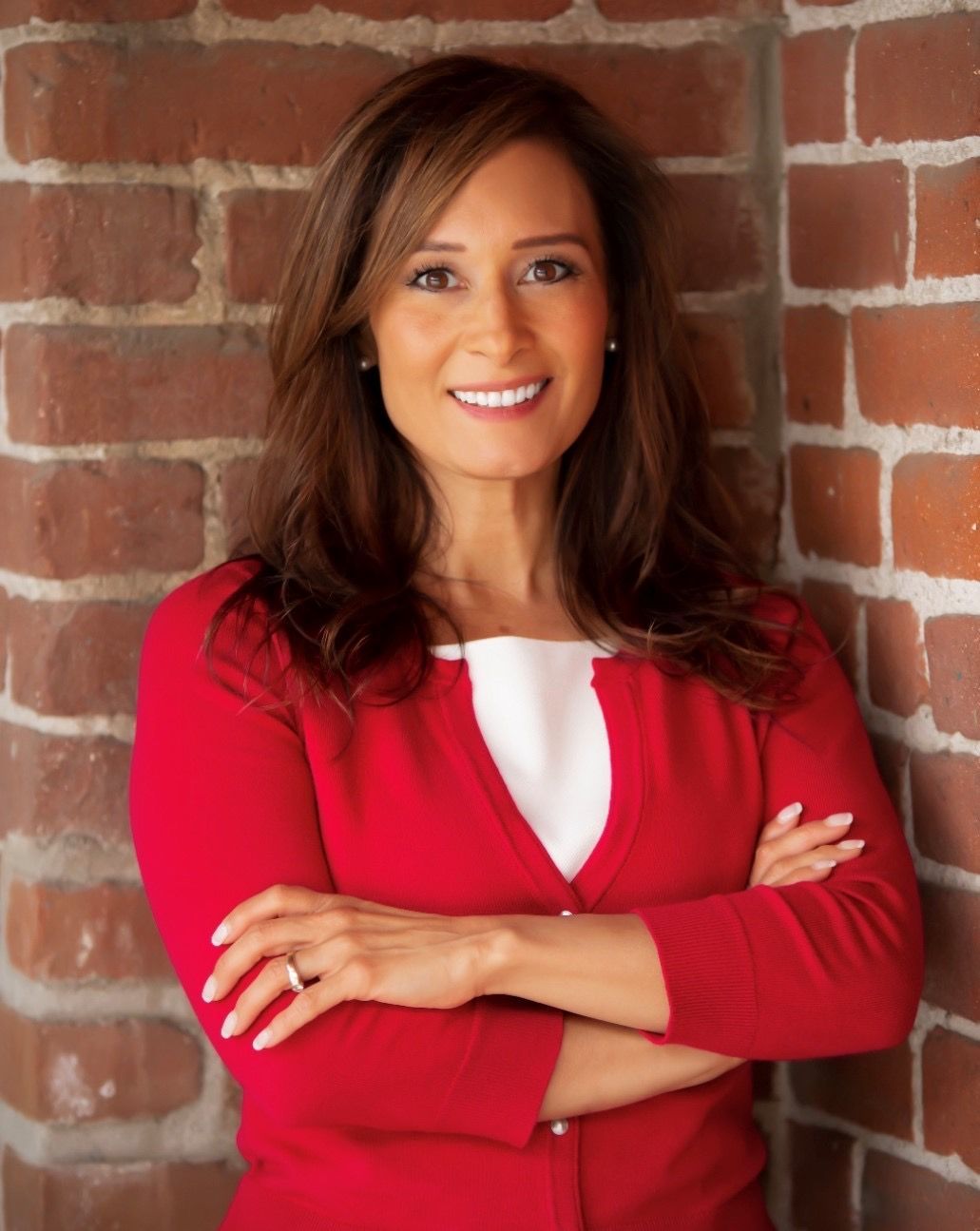 A woman in a red sweater is standing in front of a brick wall with her arms crossed