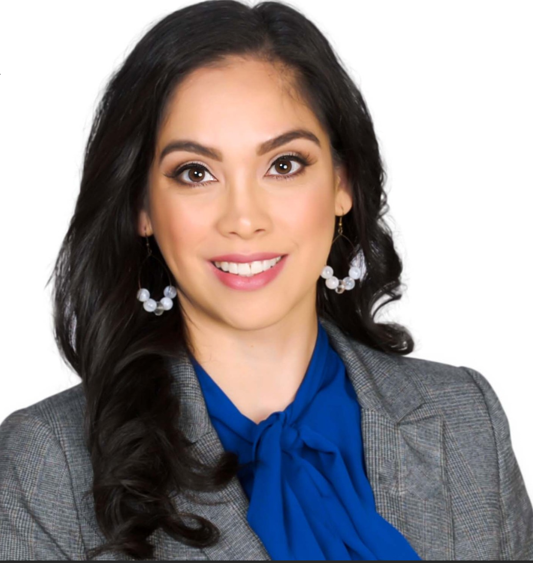 A woman wearing a gray jacket and a blue tie smiles for the camera