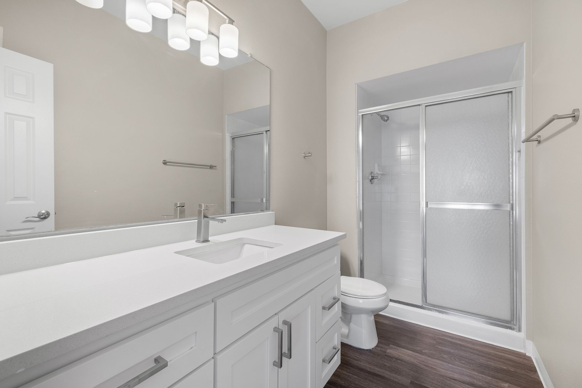 Bright modern bathroom with double vanity, large mirror, and glass-enclosed shower.