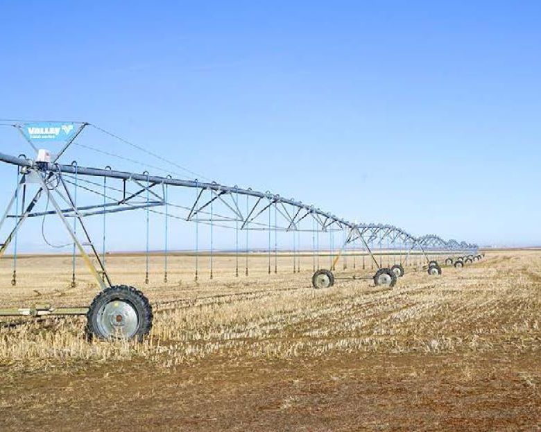 Center-pivot irrigation system in a dry, harvested field under a clear blue sky.