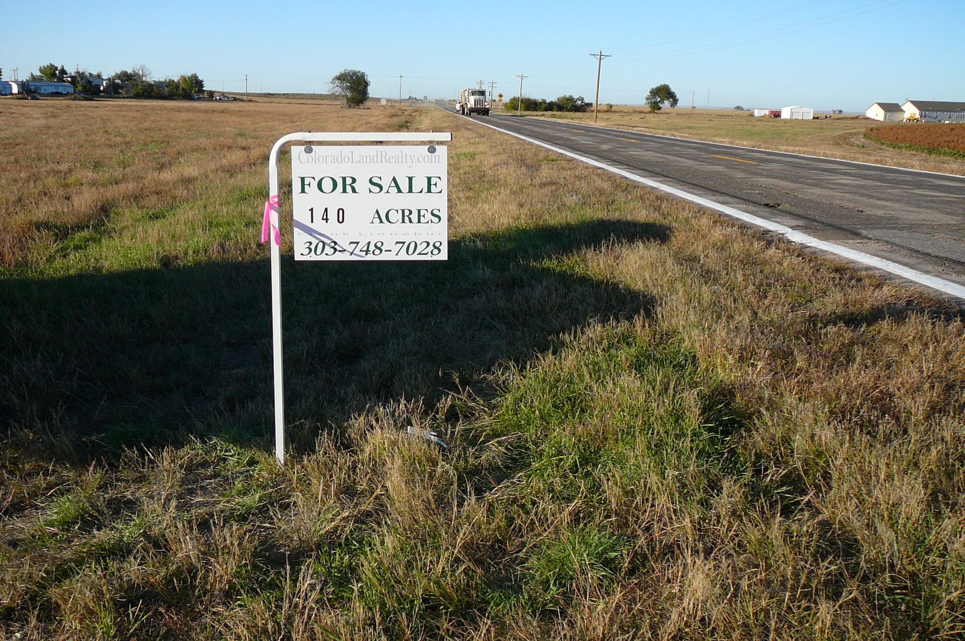 Sign for sale of 140 acres of land next to a road, with brown grass and a sunny sky.