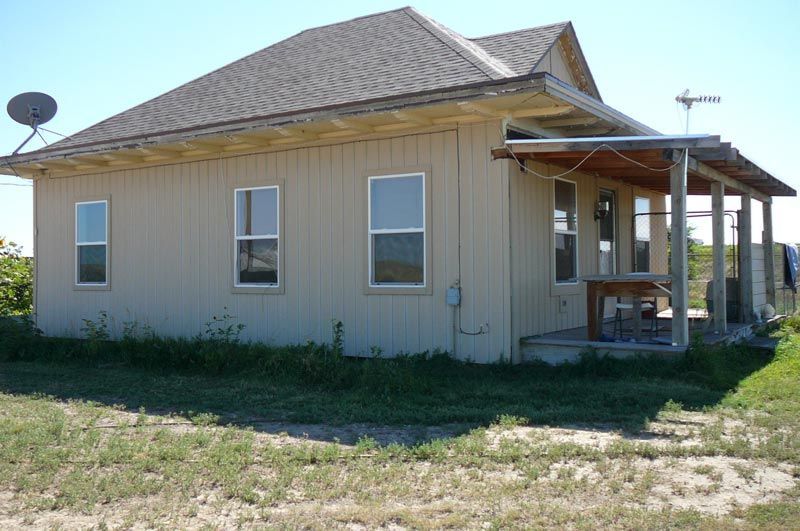 Beige house with a porch, satellite dish, and windows in a grassy setting.