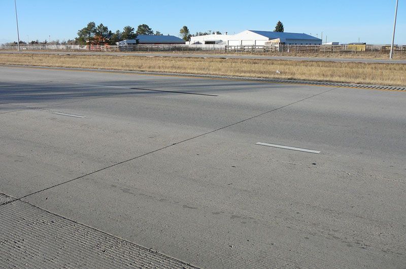 Concrete road surface with textured pattern and broken white lines, buildings in background.