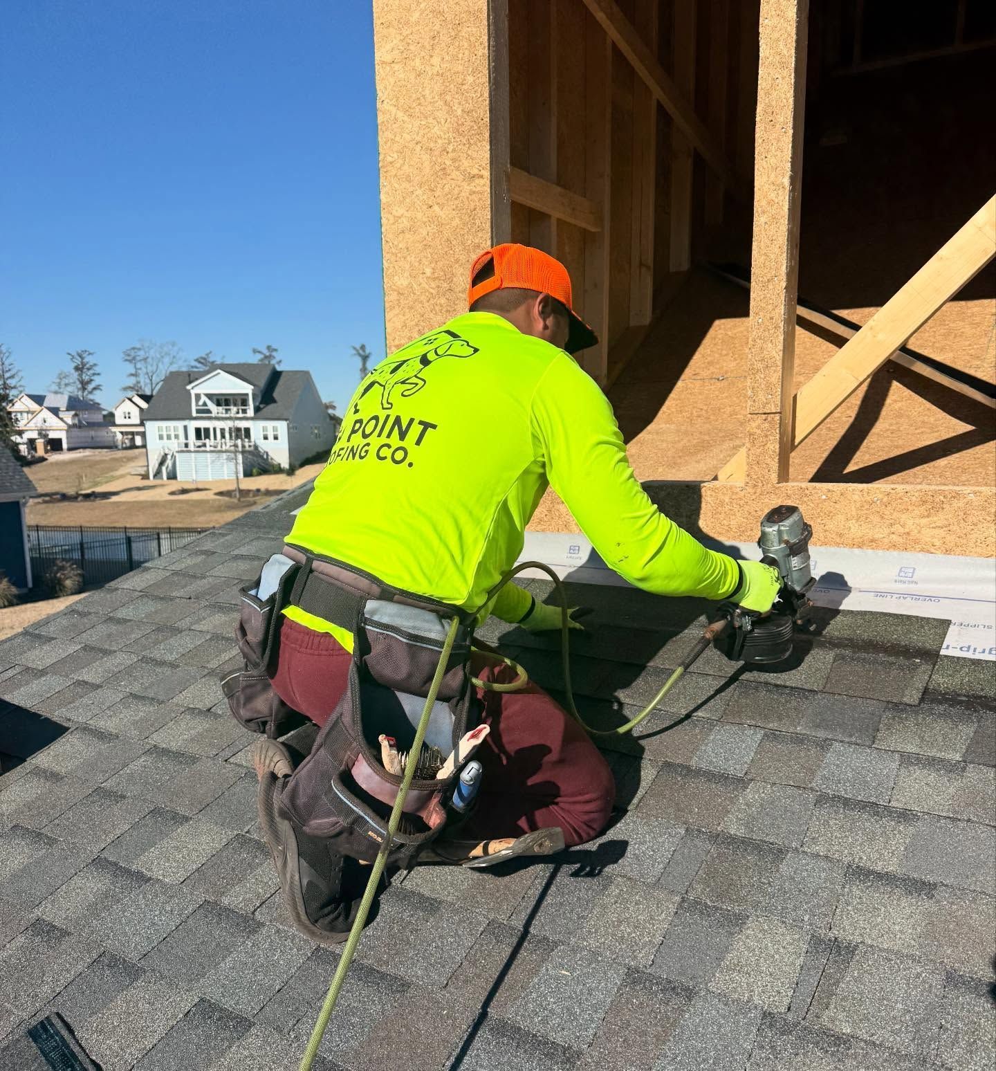 Worker in neon safety shirt securing shingles on a rooftop with a power tool