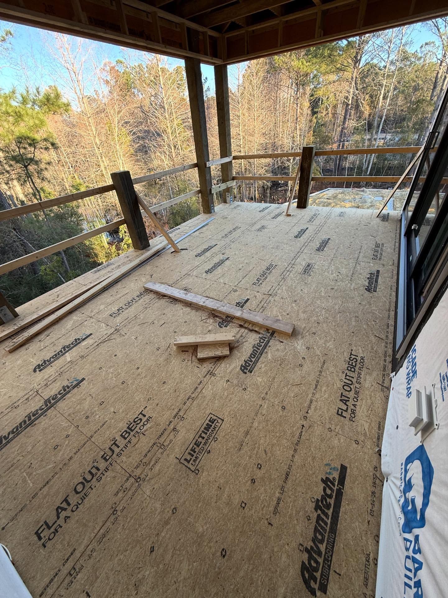 Partially built wooden porch with railing, viewed from inside, overlooking trees in autumn