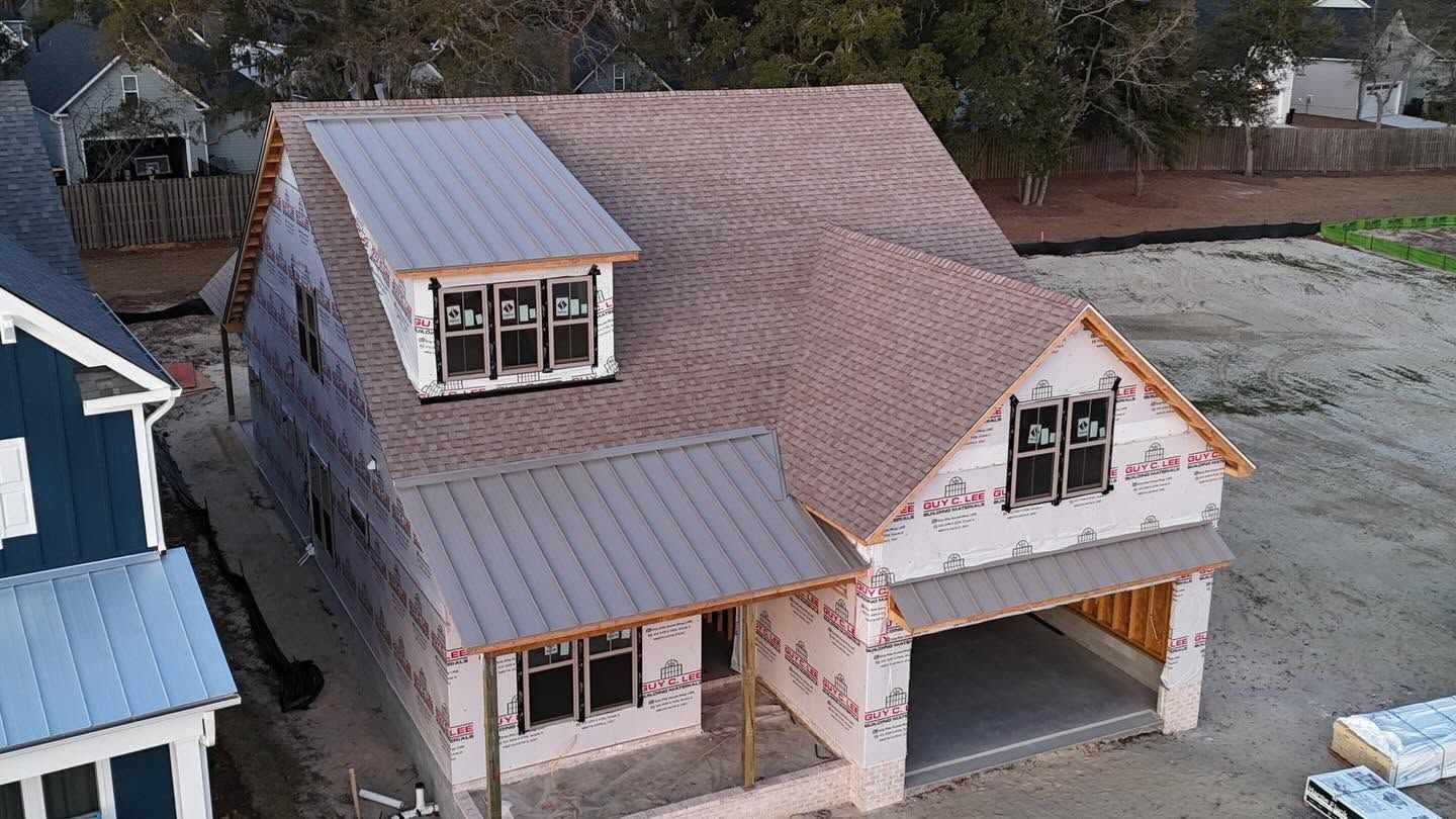 Aerial view of a partially finished two-story house with a gray roof, dormer windows, and garage.