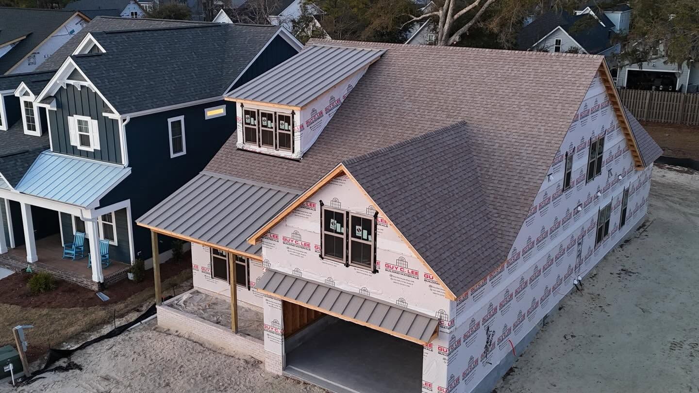 Aerial view of two houses under construction, with exposed roofs, siding, and a covered porch.