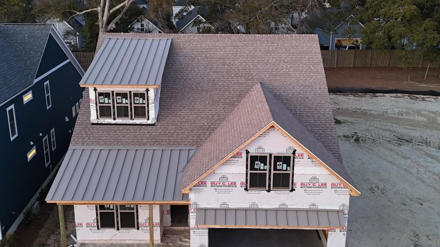 Aerial view of a house under construction with gray siding, metal roof, and exposed wrap on the front gable.