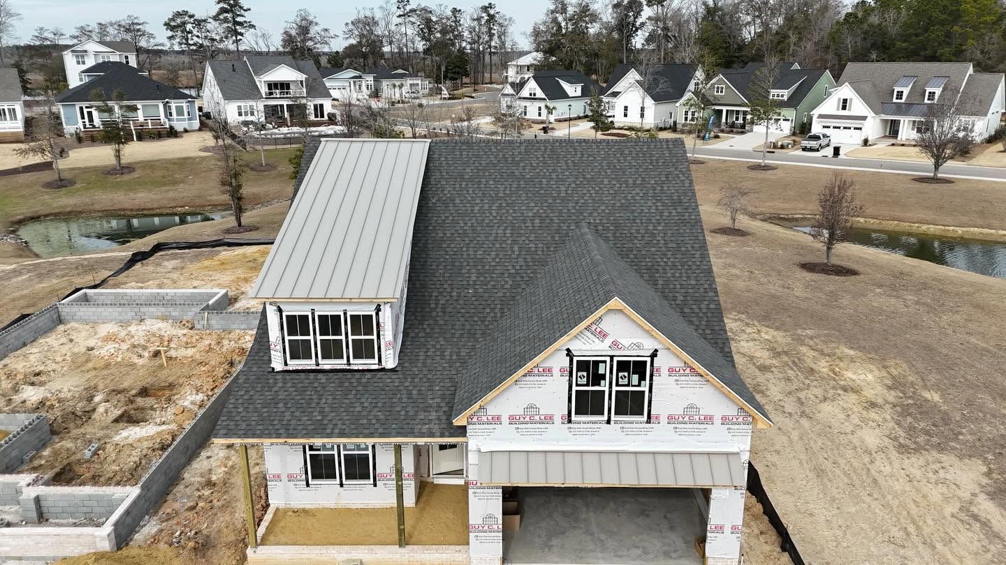 A house under construction with gray siding, roof, and garage in a suburban neighborhood.