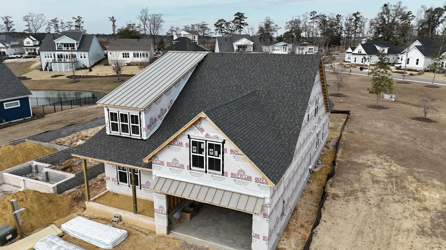 Aerial view of a house under construction with a dark roof and unfinished siding in a suburban neighborhood