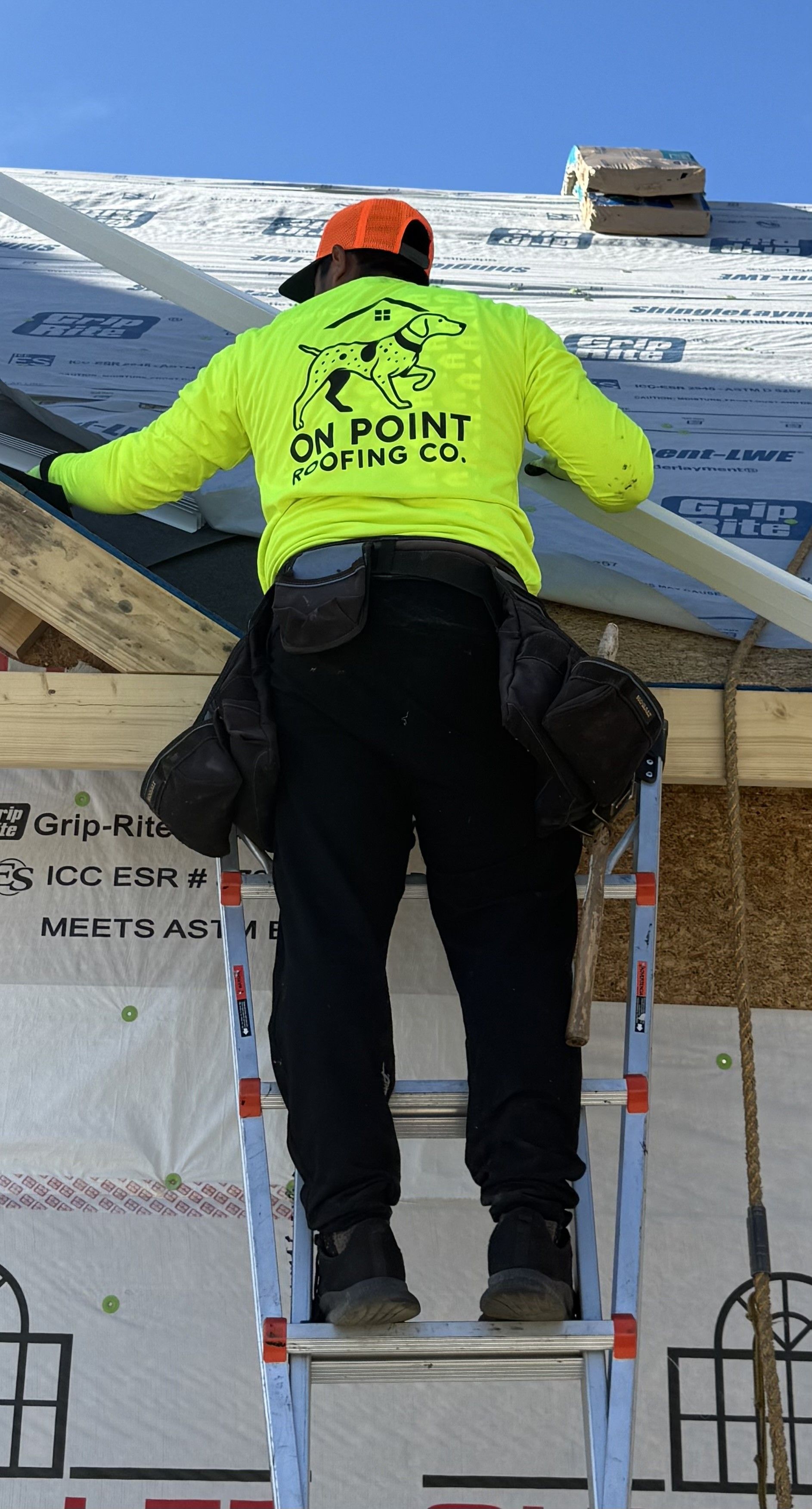 Worker on ladder installing roofing underlayment on a house under construction.