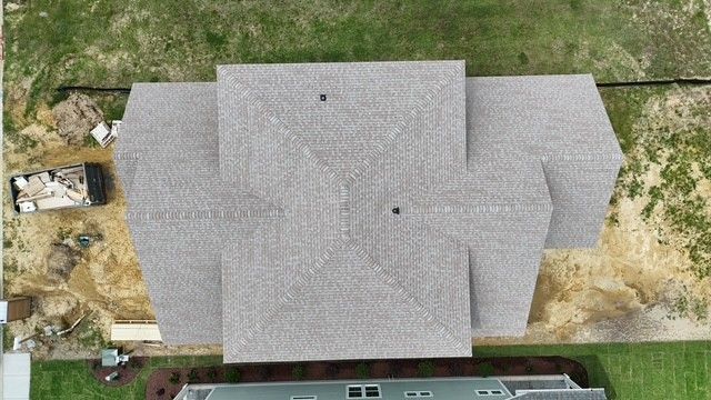 Aerial view of a gray-shingled house roof beside a grassy yard and dirt area.